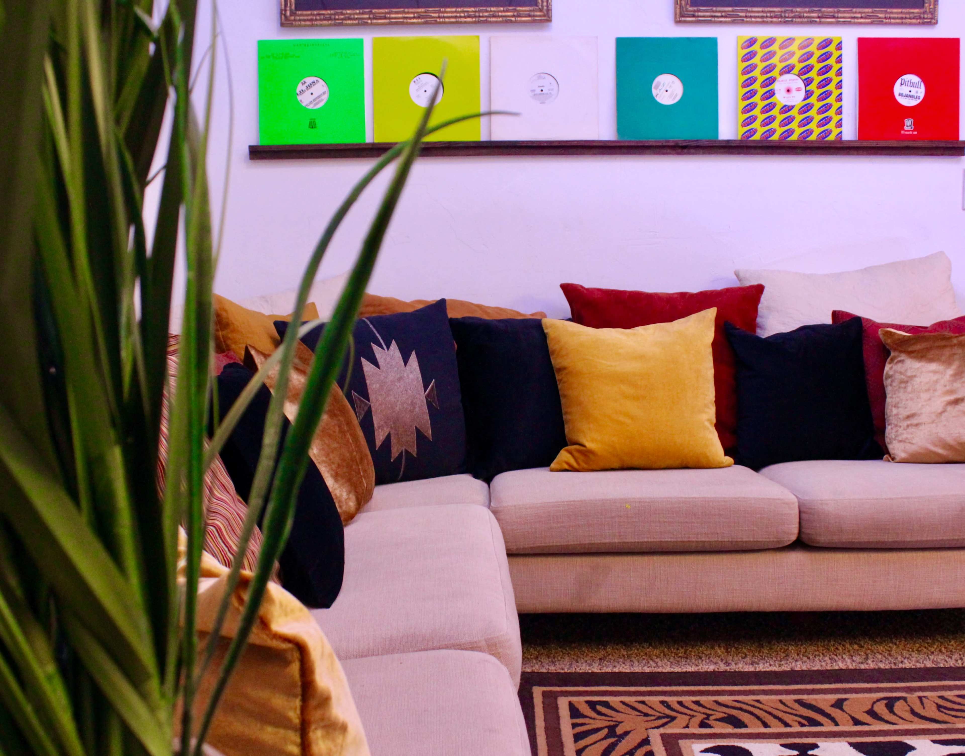 A beige couch with multiple colorful pillows is positioned in a room featuring framed vinyl records on the wall.