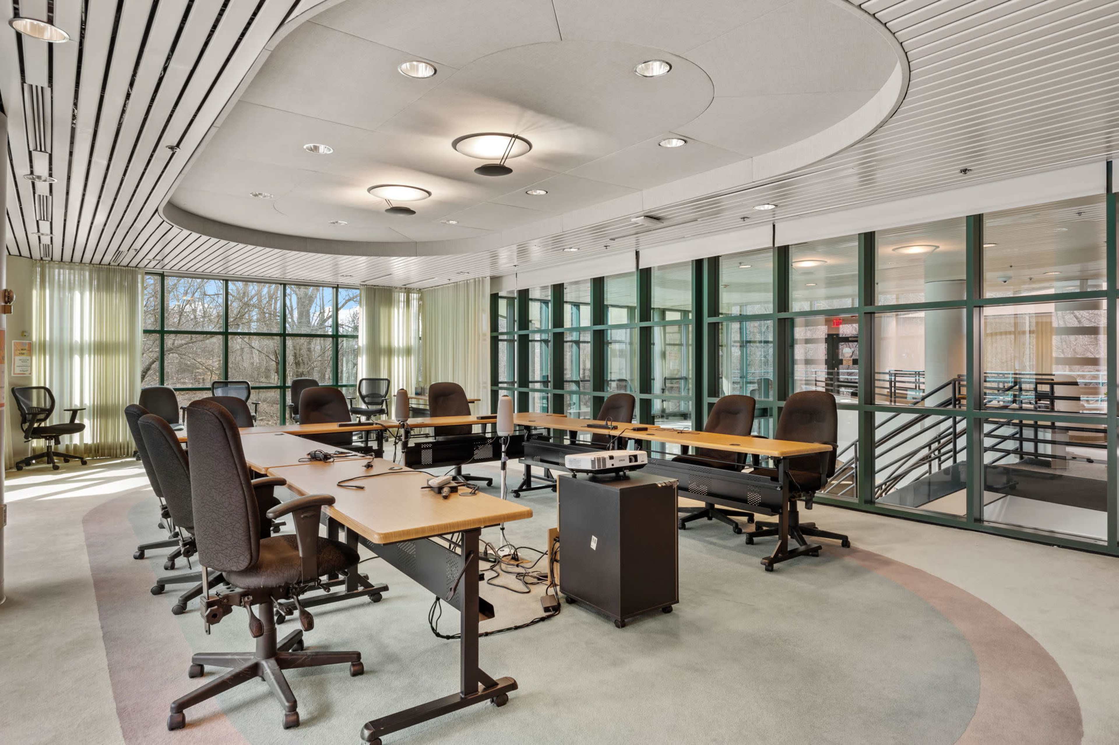 A modern conference room features a circular table surrounded by ergonomic chairs and large windows.