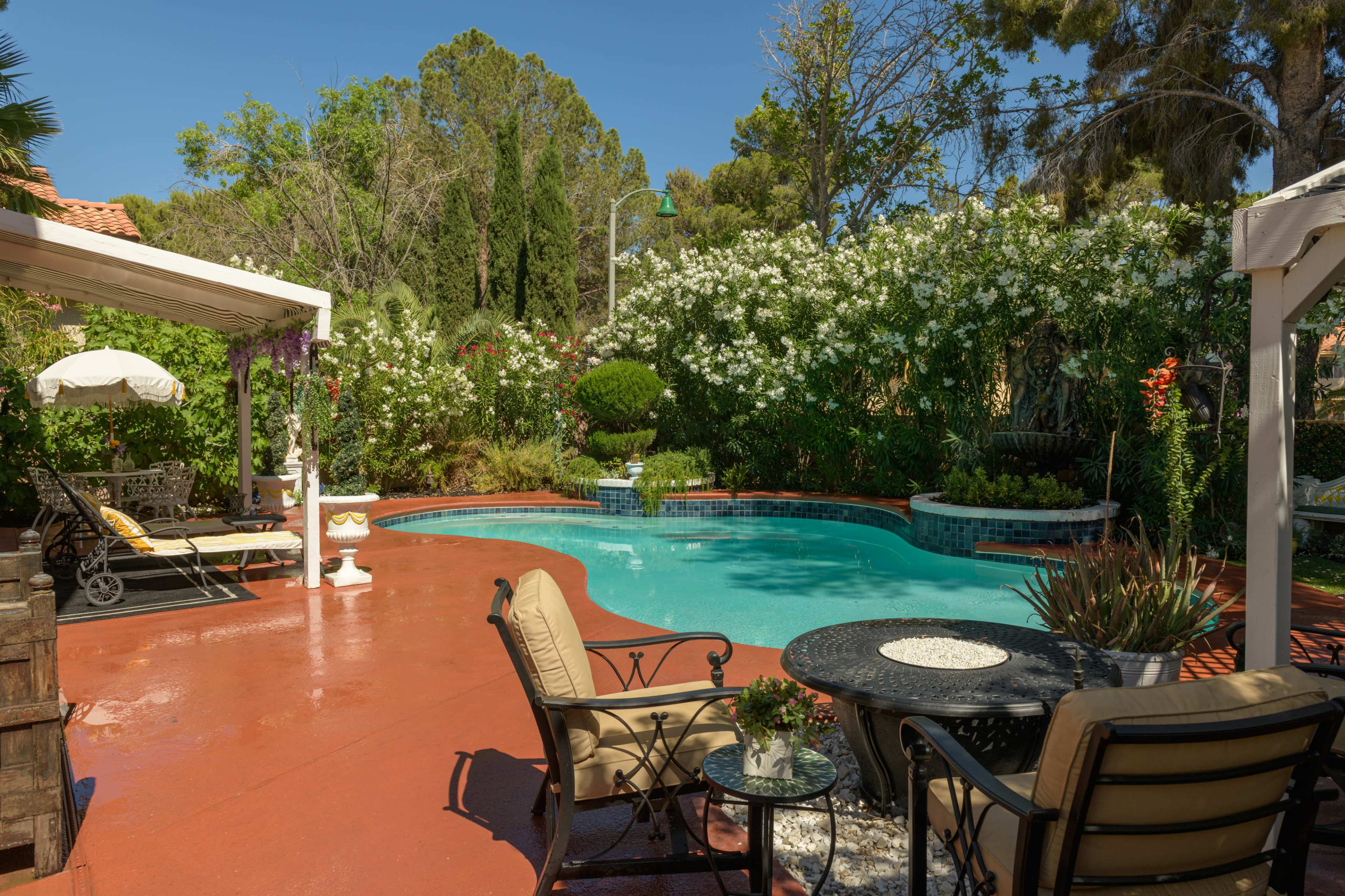 A backyard landscape features a swimming pool surrounded by green foliage and outdoor seating.