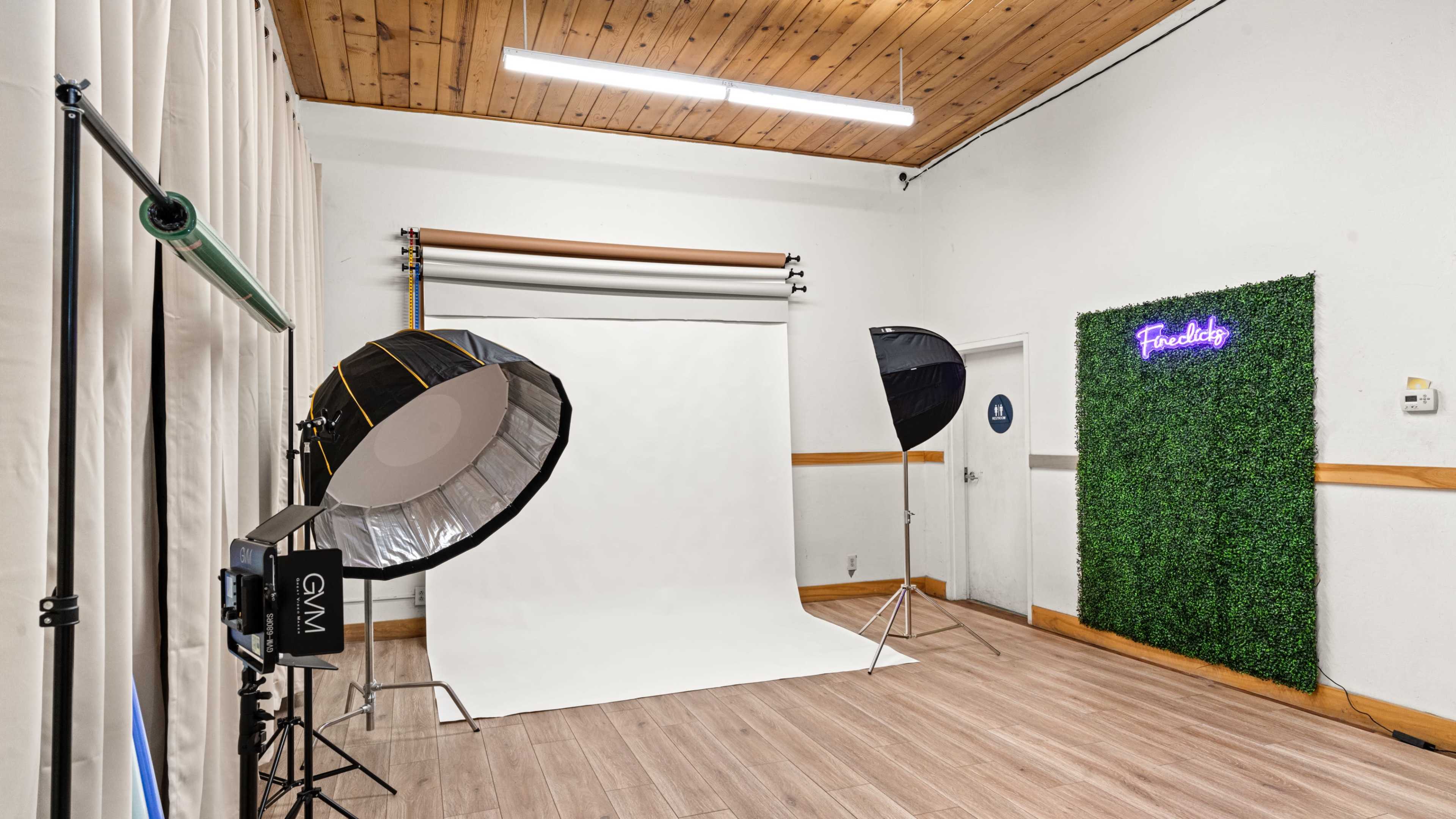 The image shows a photography studio with a large white backdrop, lighting equipment, and a green wall featuring the word "Freedom" in neon lights.