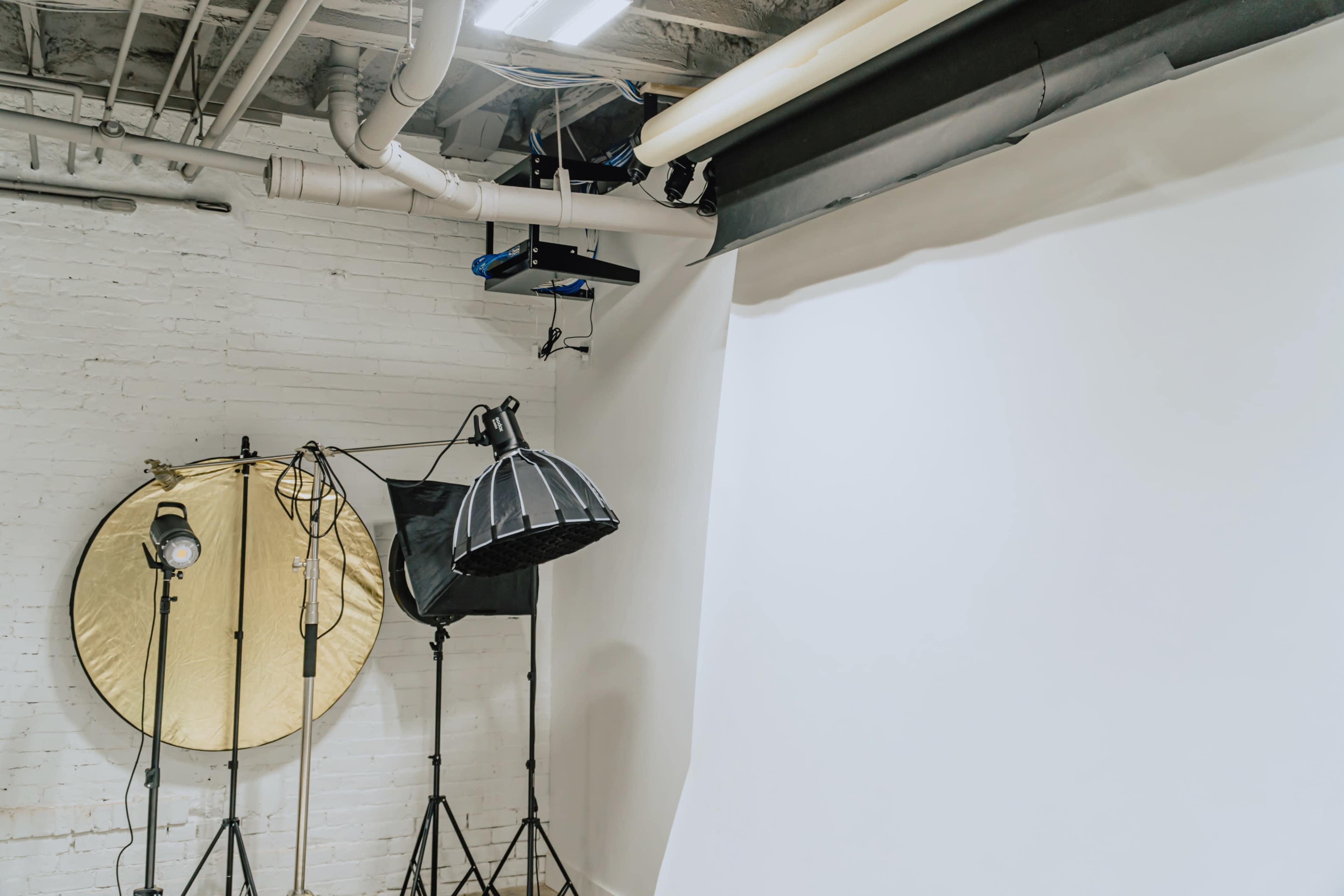 A photography studio equipped with a white backdrop, lighting fixtures, and a reflective umbrella.