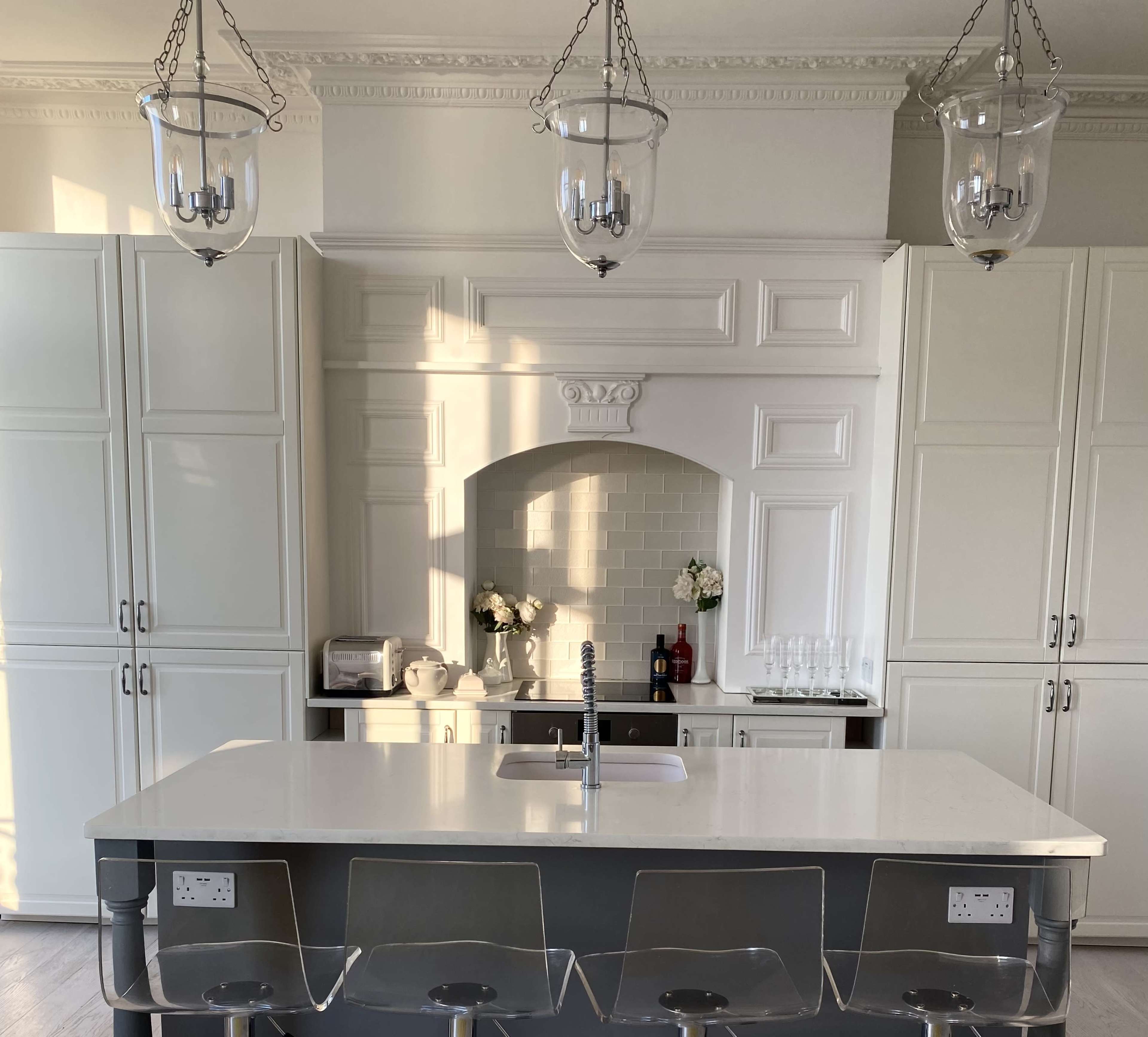 The image shows a modern kitchen with white cabinetry, a central island with a sink, and pendant lights hanging above.