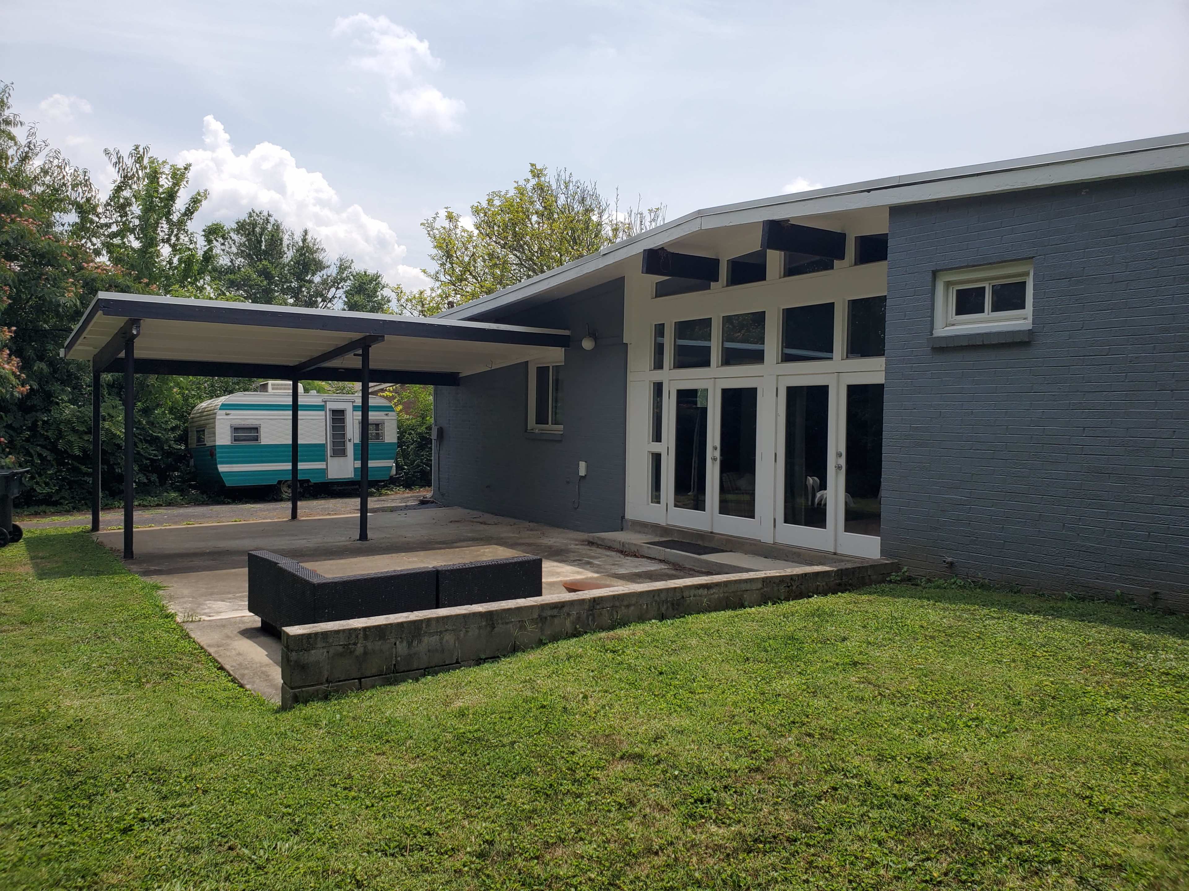 A modern house with a large patio, a covered carport, and a vintage trailer parked in the background.