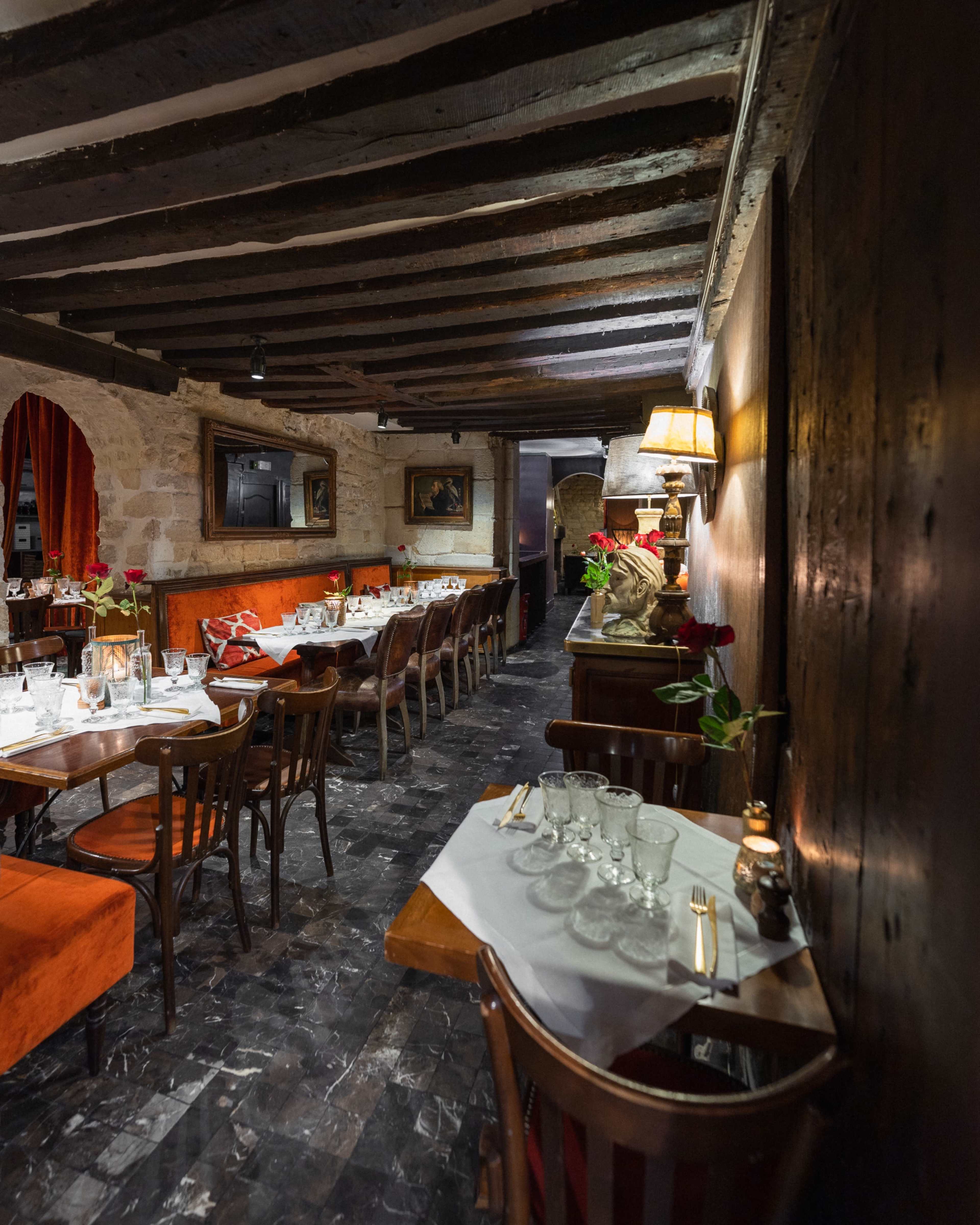 The image shows a cozy restaurant interior with wooden beams, tables set with glassware, and red roses as centerpieces.