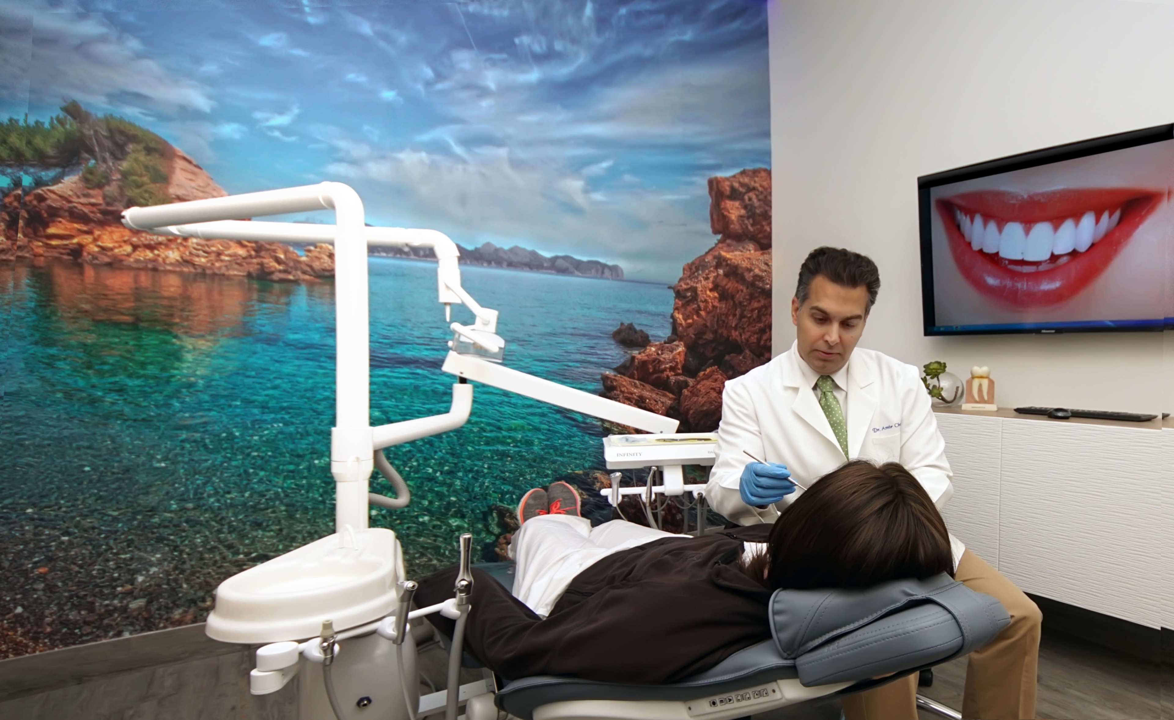 A dentist consults a patient in a modern dental clinic featuring a coastal mural on the wall.