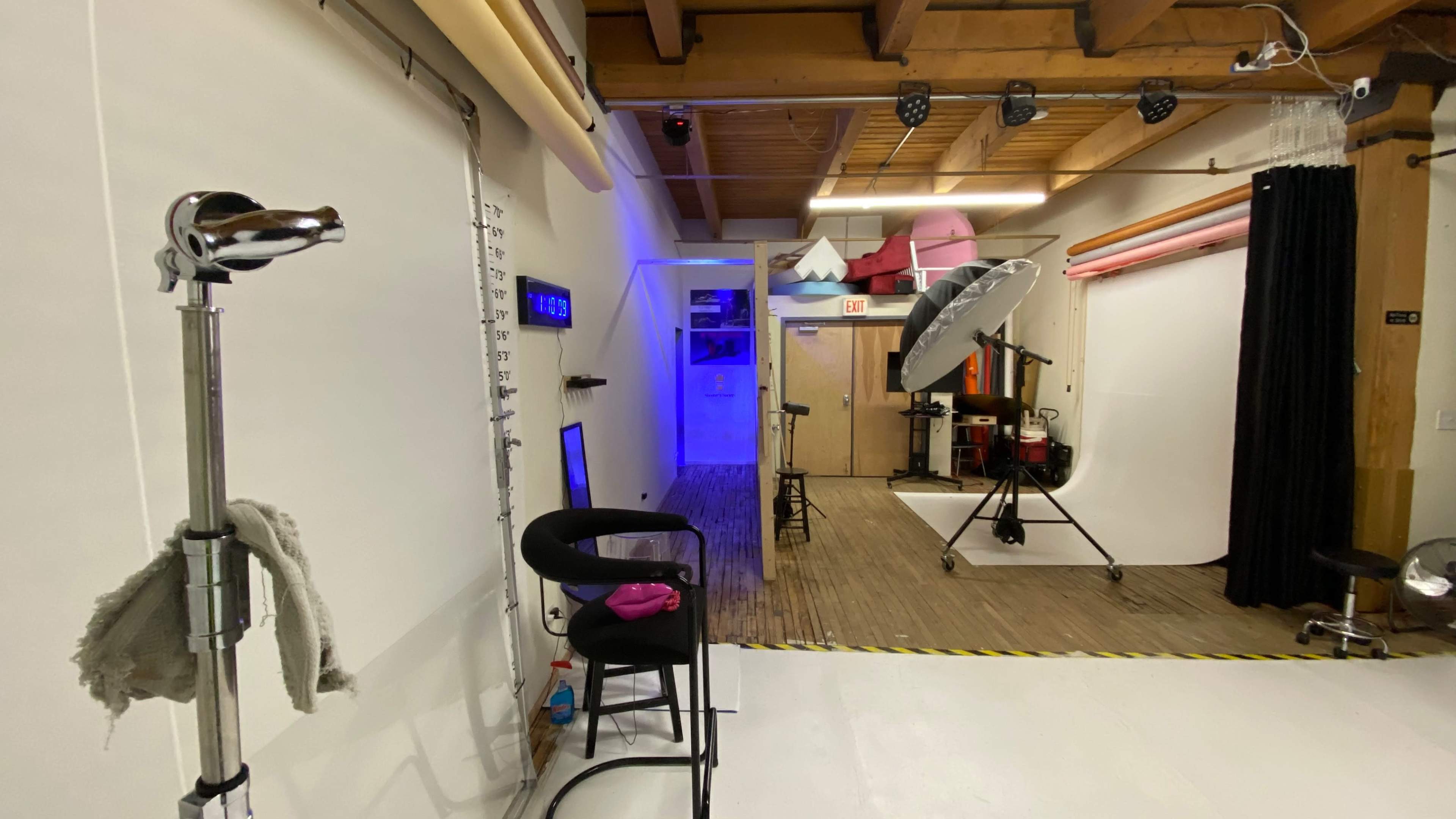 A photography studio with various equipment, including a large umbrella light, backdrop setup, and a few chairs arranged around the space.