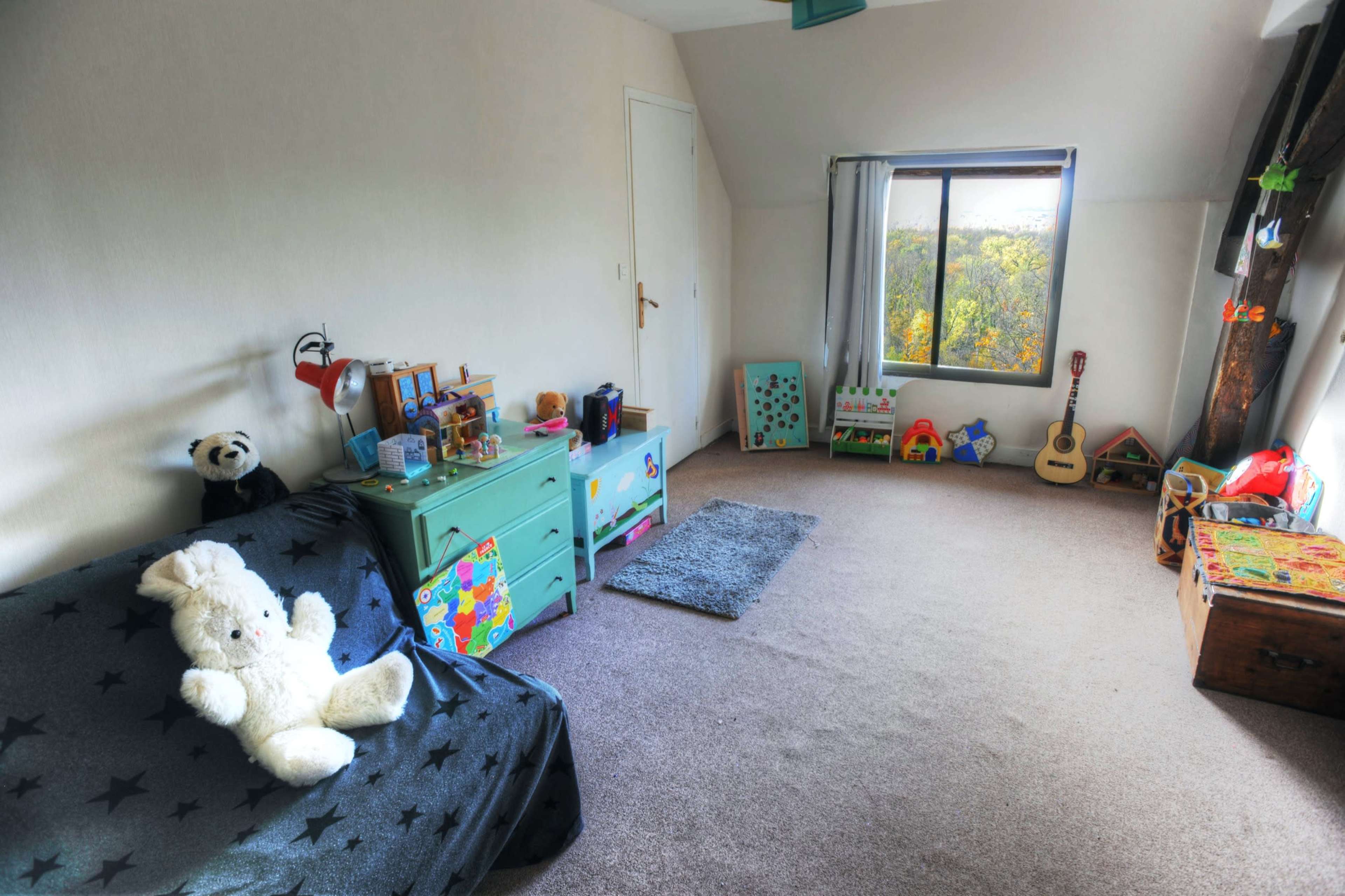The room features a low bed covered with a black star-patterned blanket, a green dresser, and various toys arranged around a window overlooking greenery.