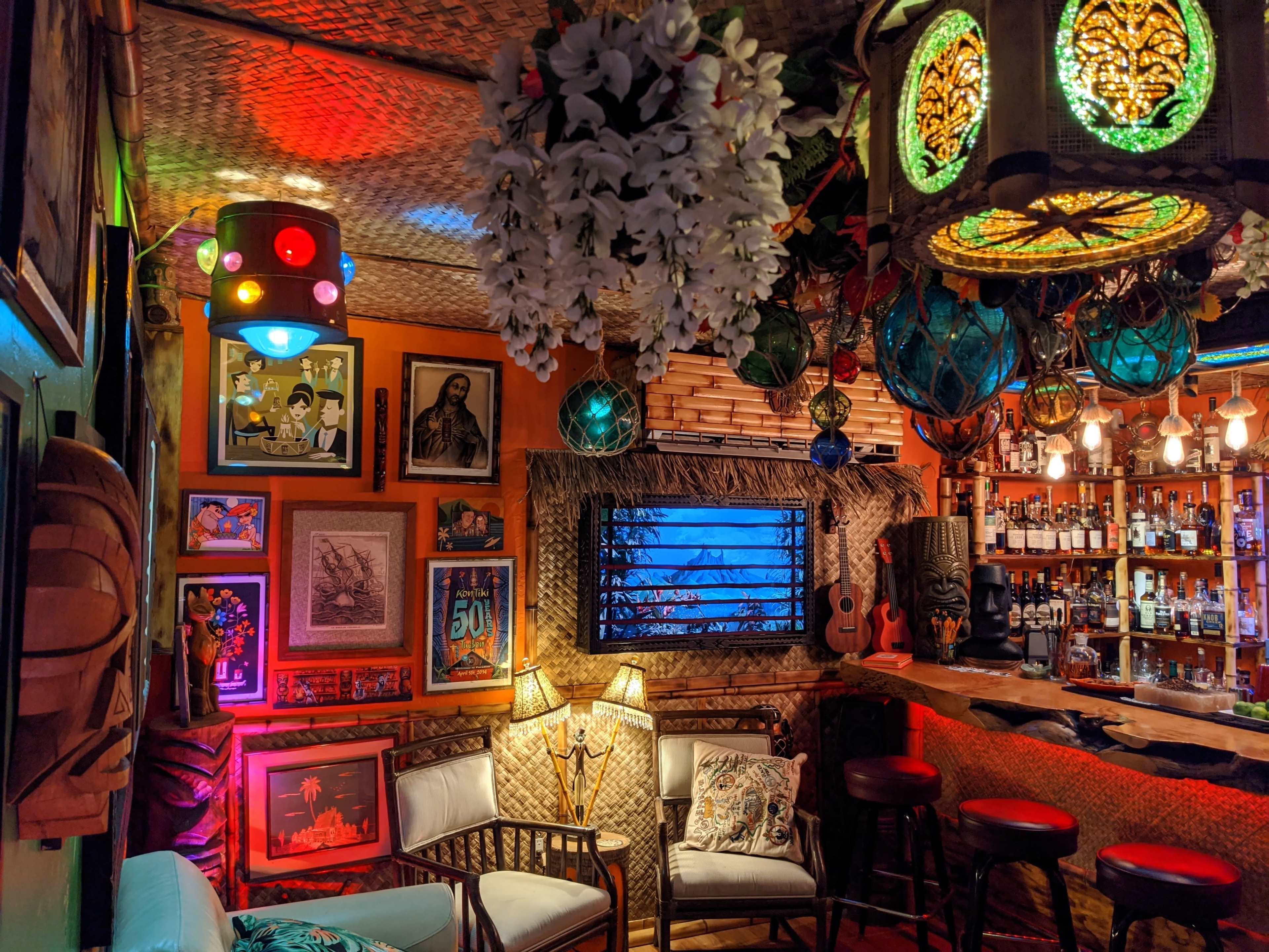 The image shows a vibrant bar interior with eclectic decor, including colorful lights, various artworks on the walls, and a well-stocked bar in the background.