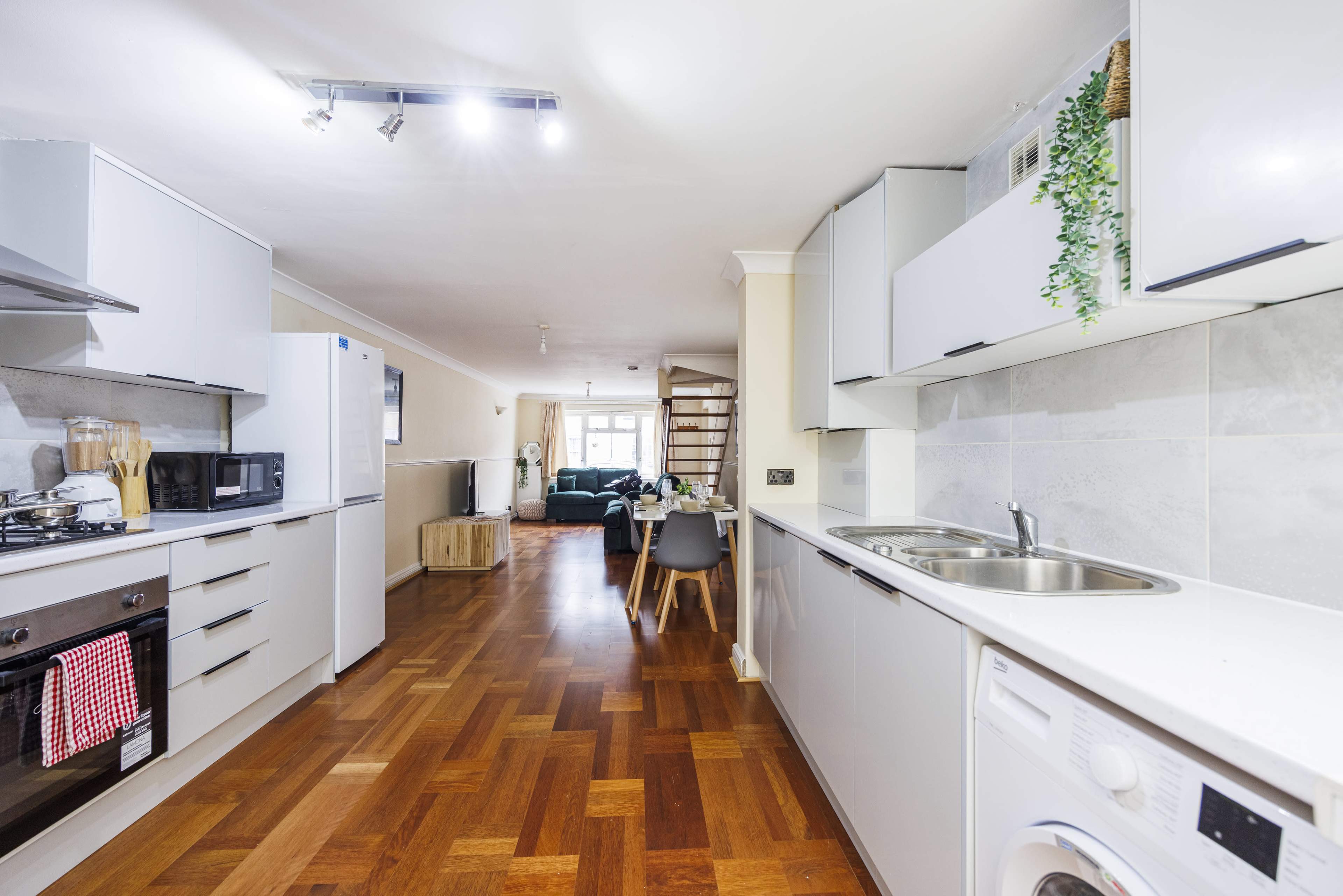 A modern kitchen with white cabinetry, a wooden floor, and an open layout that leads to a living area.