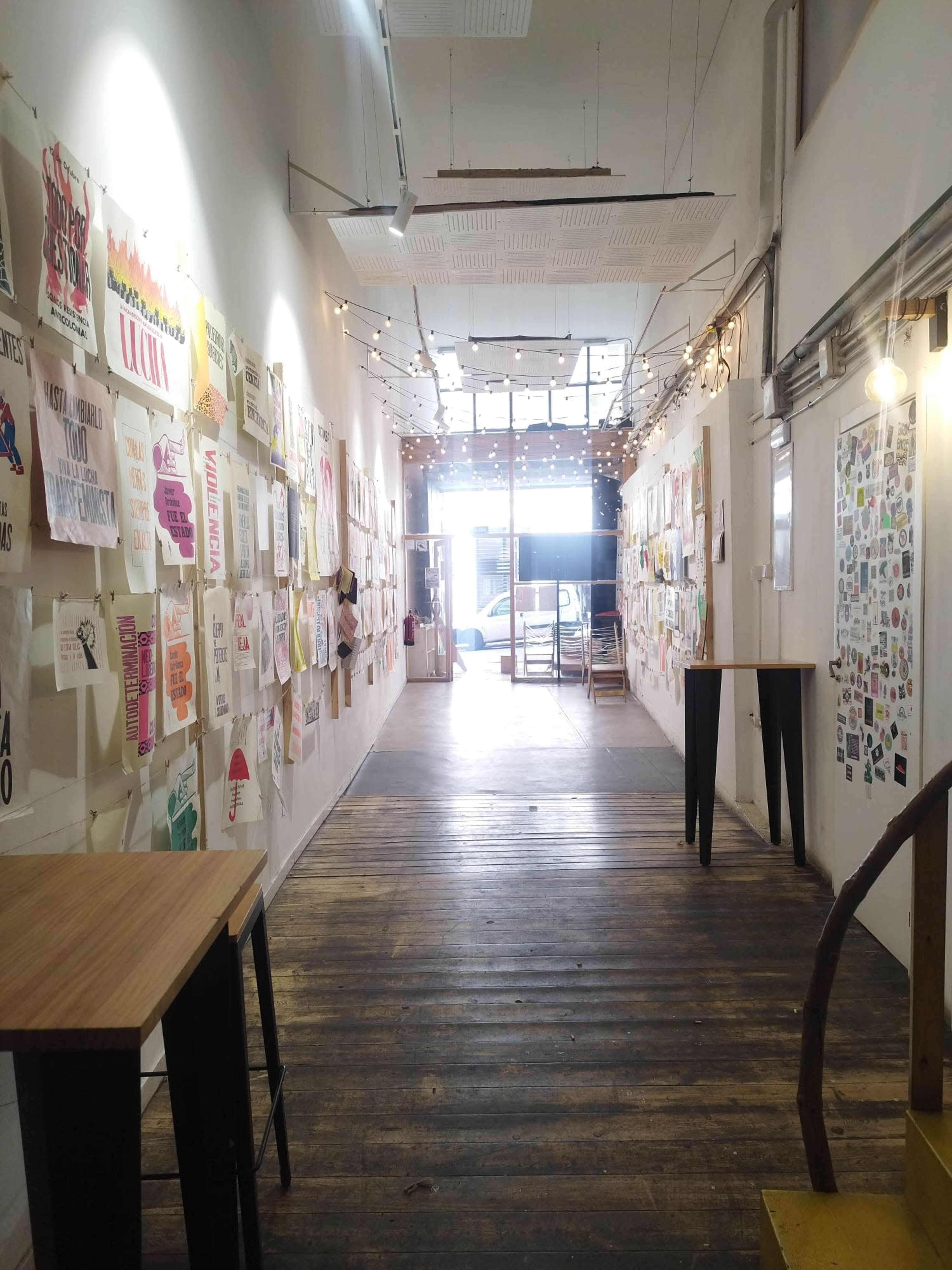 The image shows a long hallway lined with various posters and art prints, leading to a brightly lit entrance.