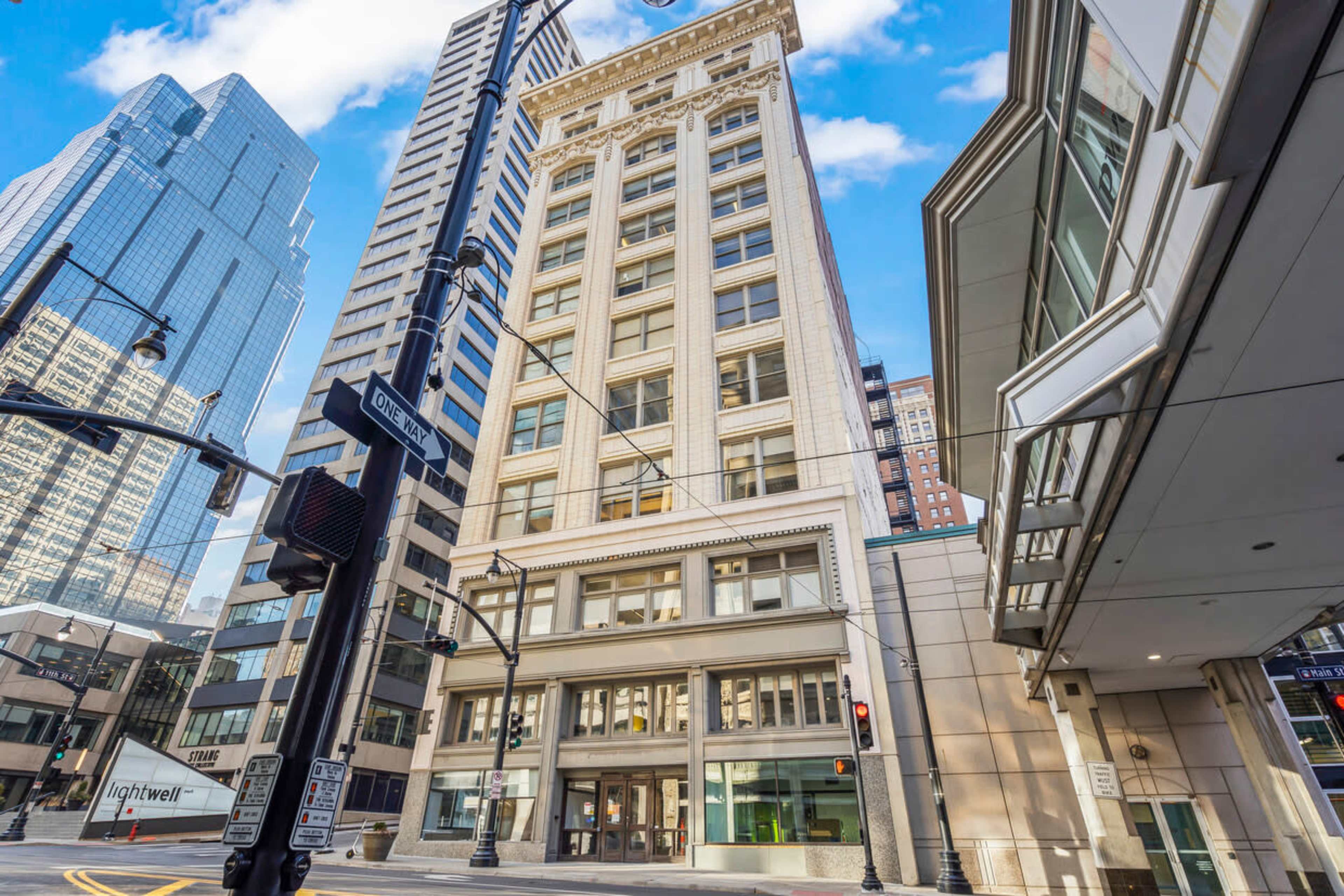 A tall building with a classic facade positioned at the intersection of two city streets, surrounded by modern skyscrapers.