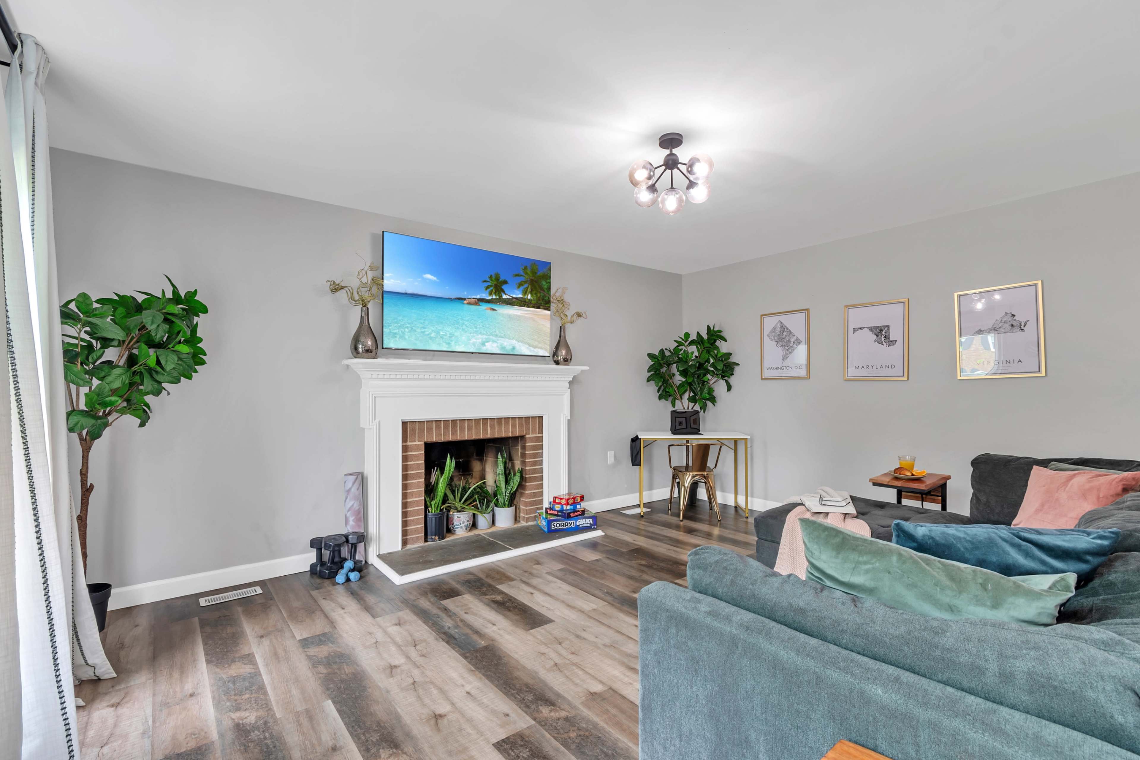 The living room features a TV mounted above a fireplace, surrounded by plants and decorative artwork on the walls.