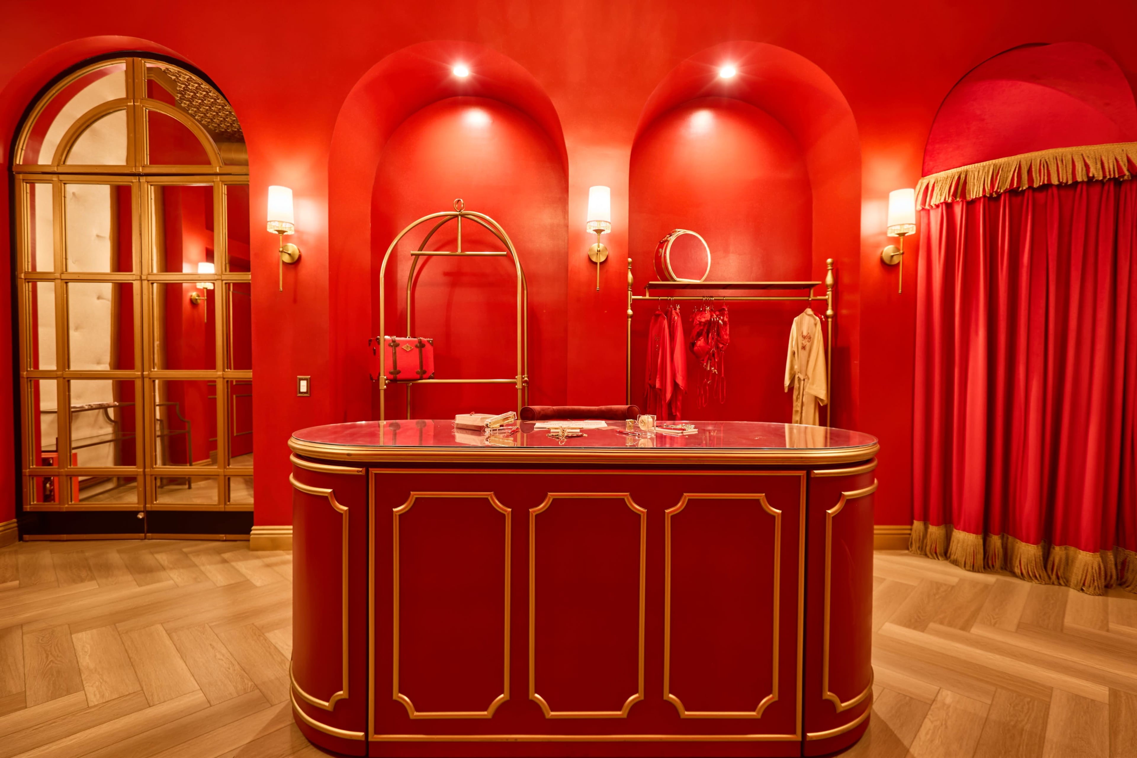 The image shows a boutique interior with a red color scheme, featuring a curved reception desk, clothing displays, and elegant wall sconces.