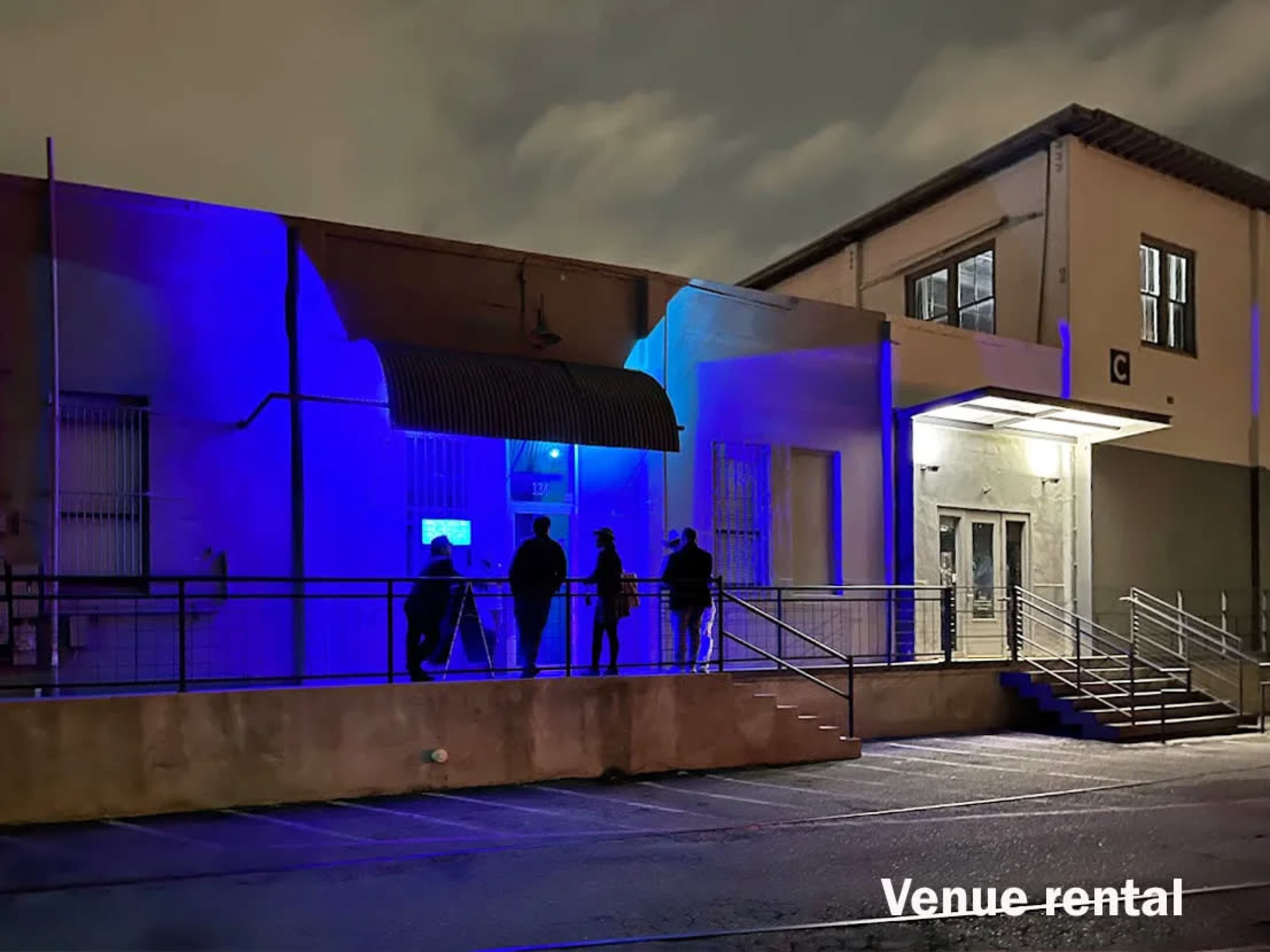 A group of people stands outside a building illuminated by blue lighting at night.