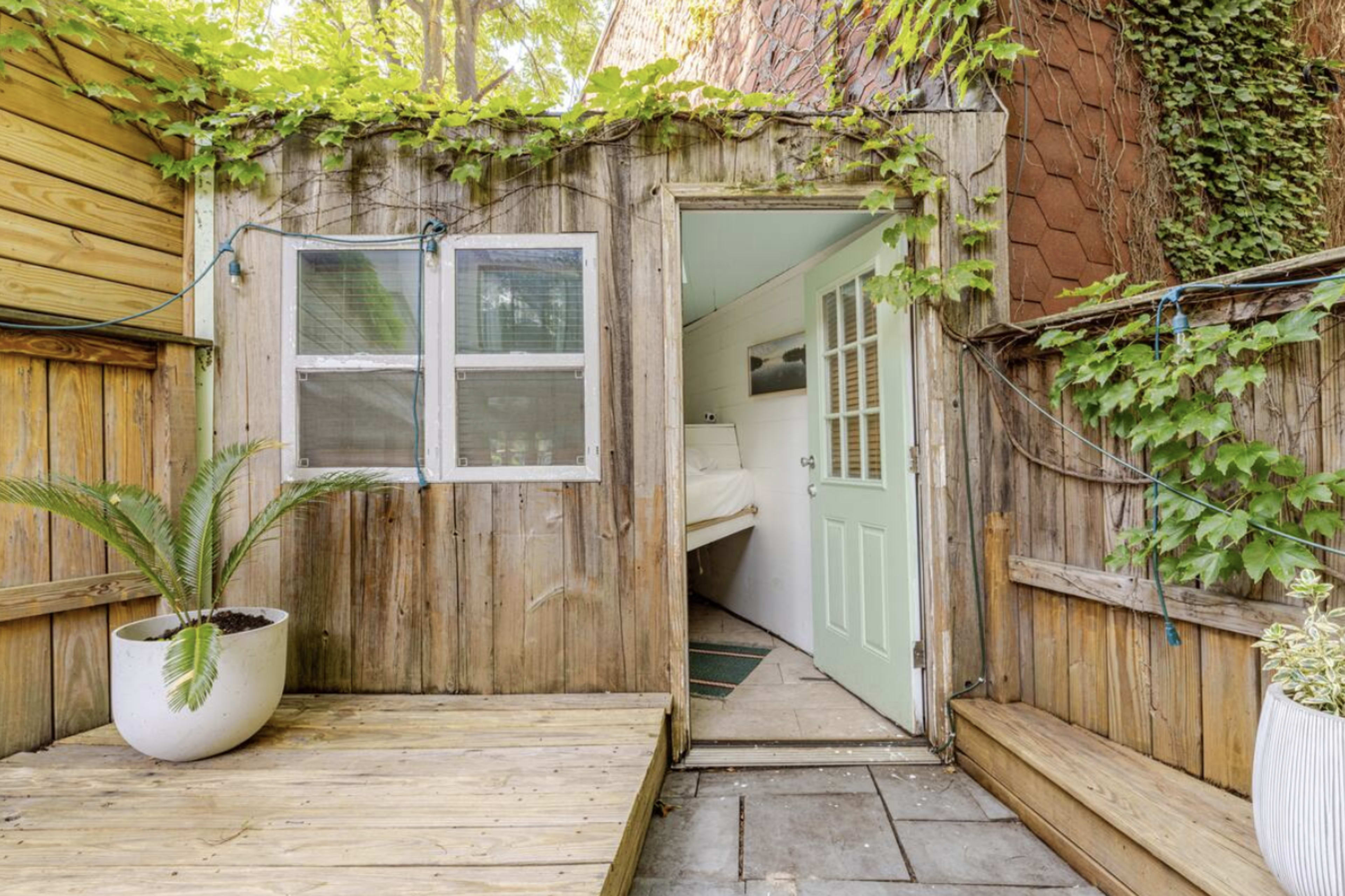 A wooden deck leads to a small entrance framed by climbing vines and a light green door.