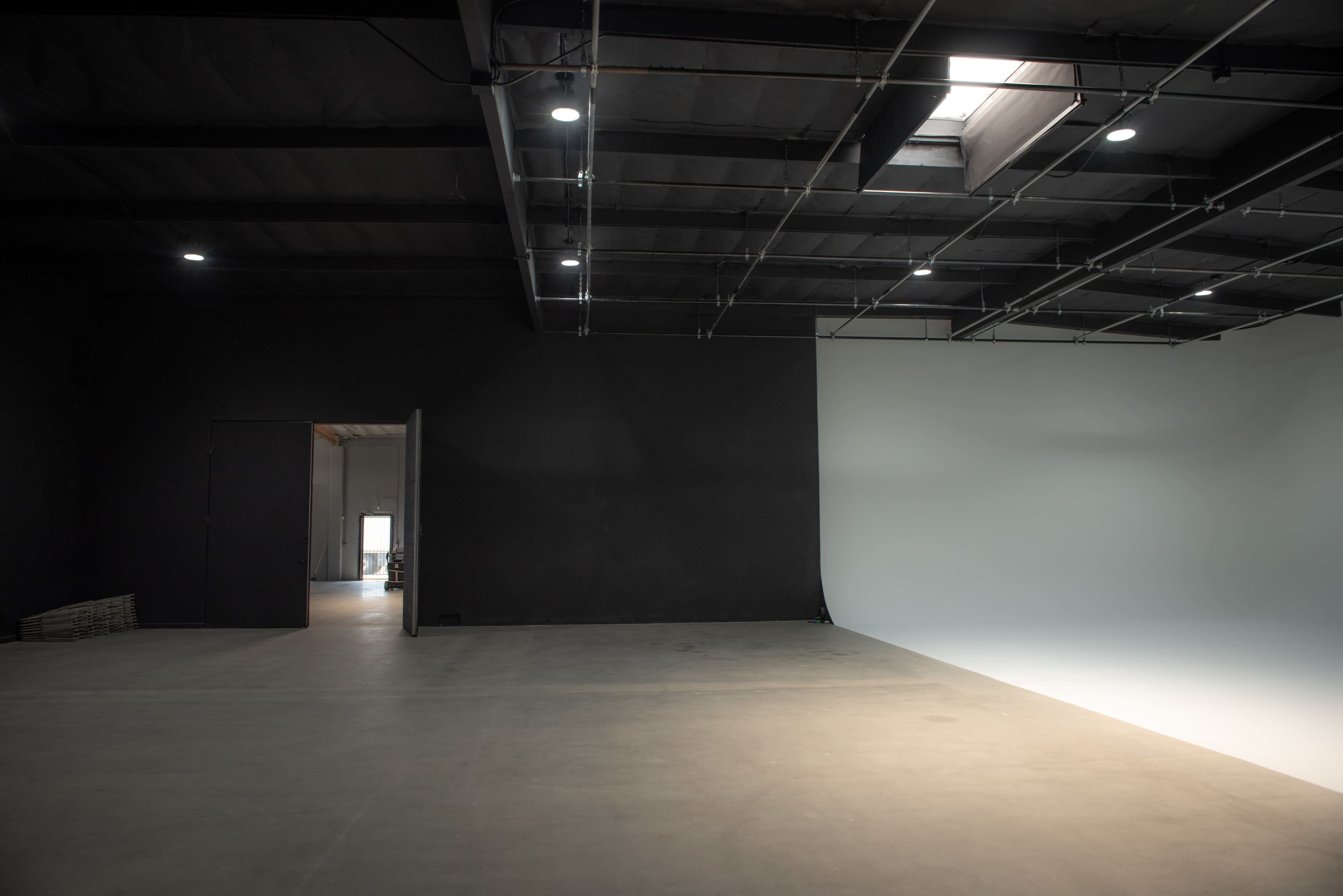 A spacious studio with a black wall on one side and a white wall on the other, lit by overhead lights.
