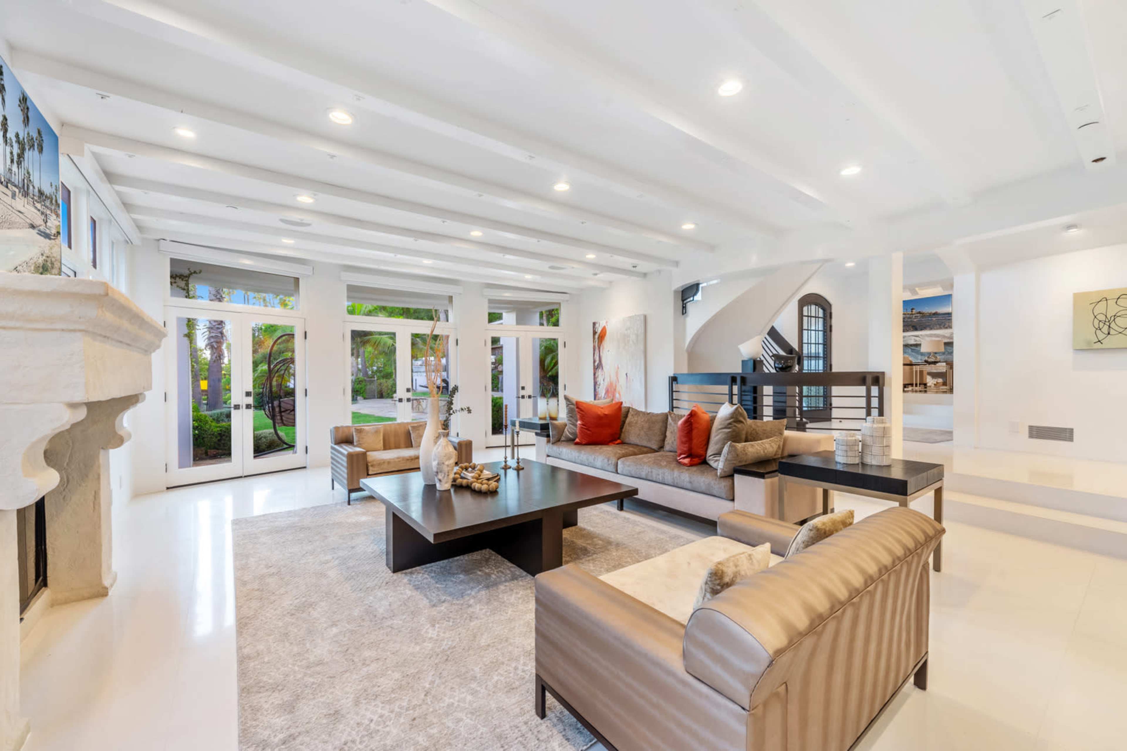 The photo shows a spacious living room featuring a large seating area with a central coffee table and large glass doors opening to a patio with palm trees.