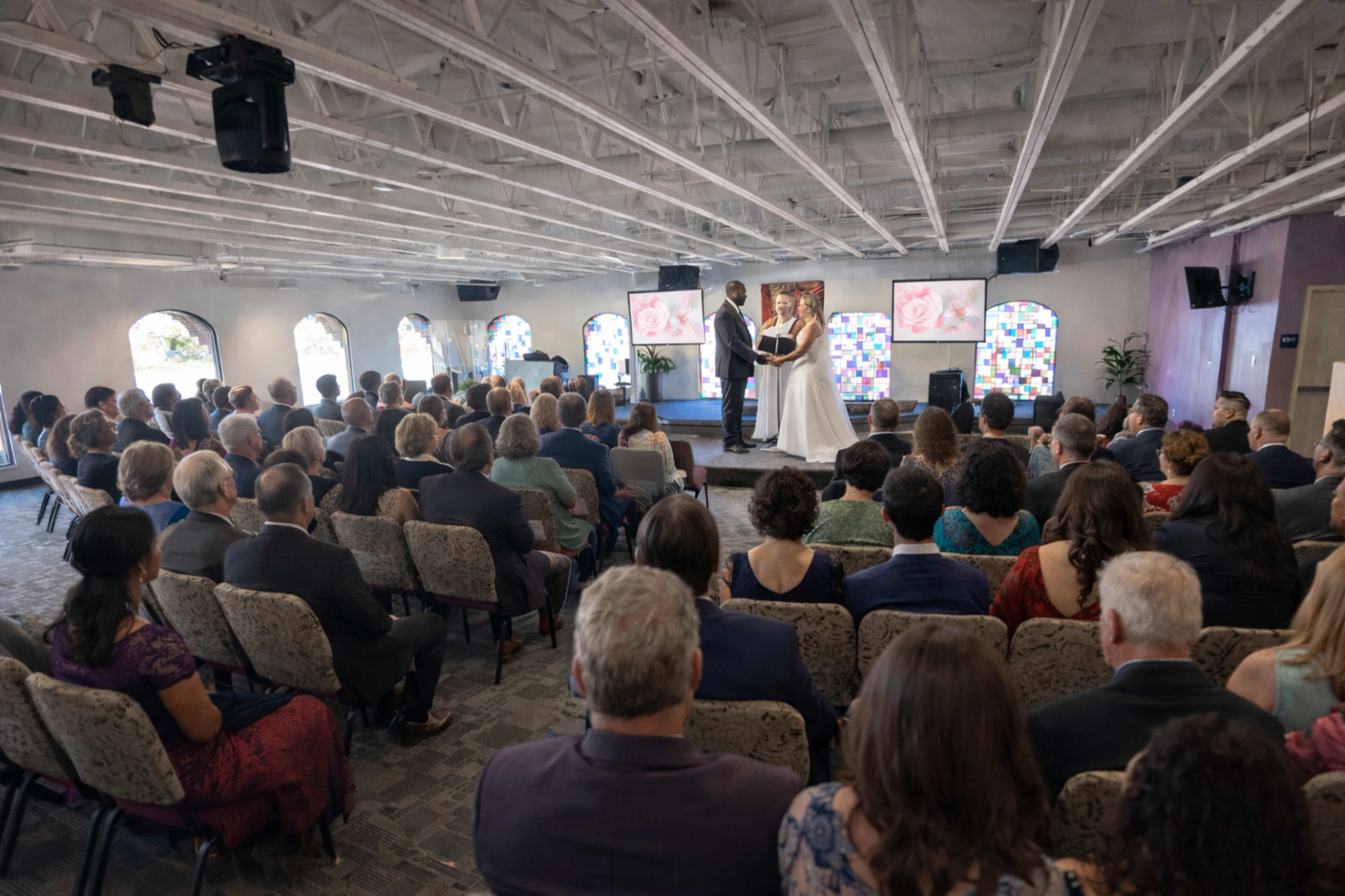 A couple exchanges vows during a wedding ceremony held in a large indoor venue filled with seated guests.