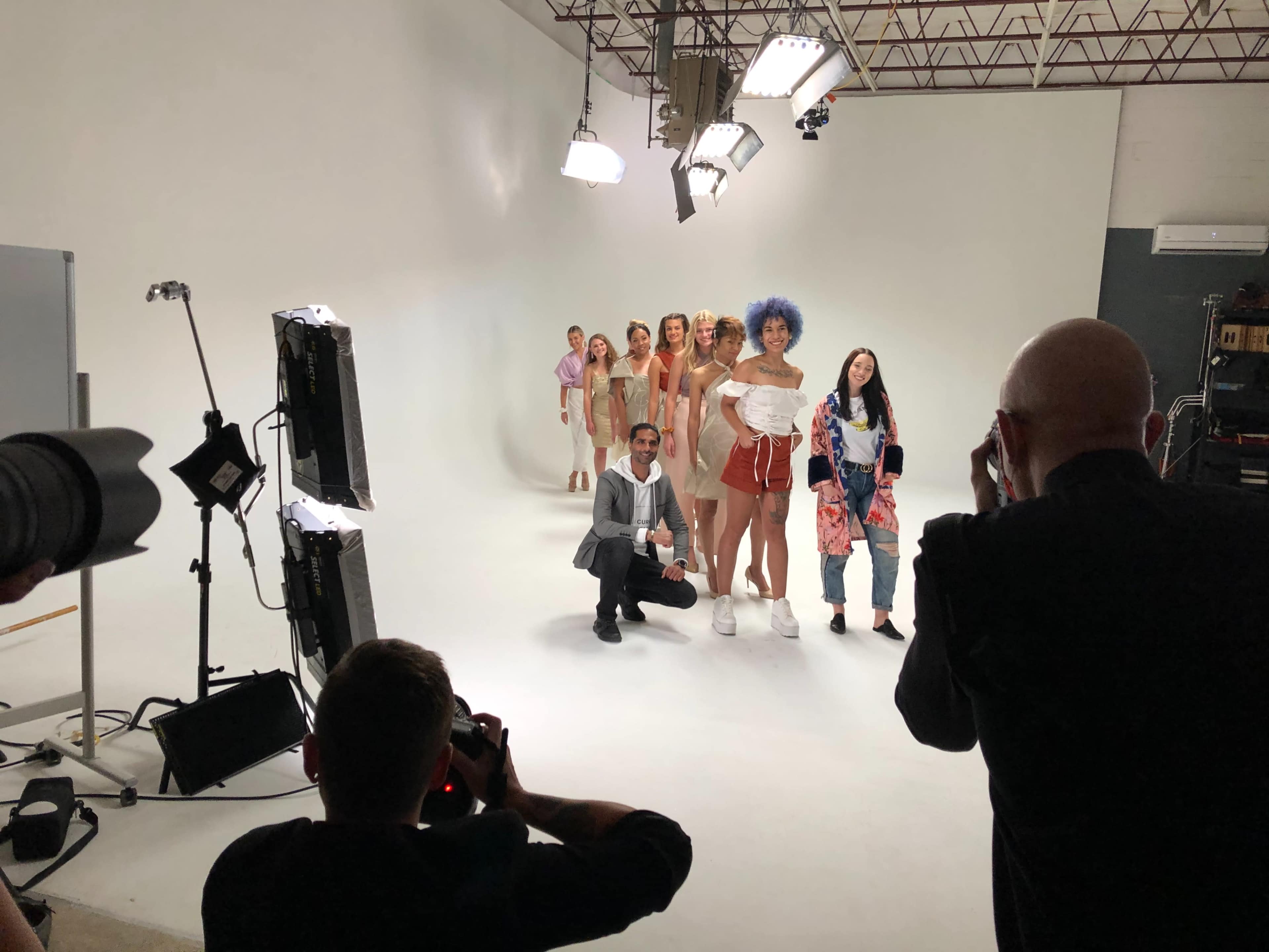 A group of models poses for a photo shoot in a studio with bright lighting and a seamless white backdrop.