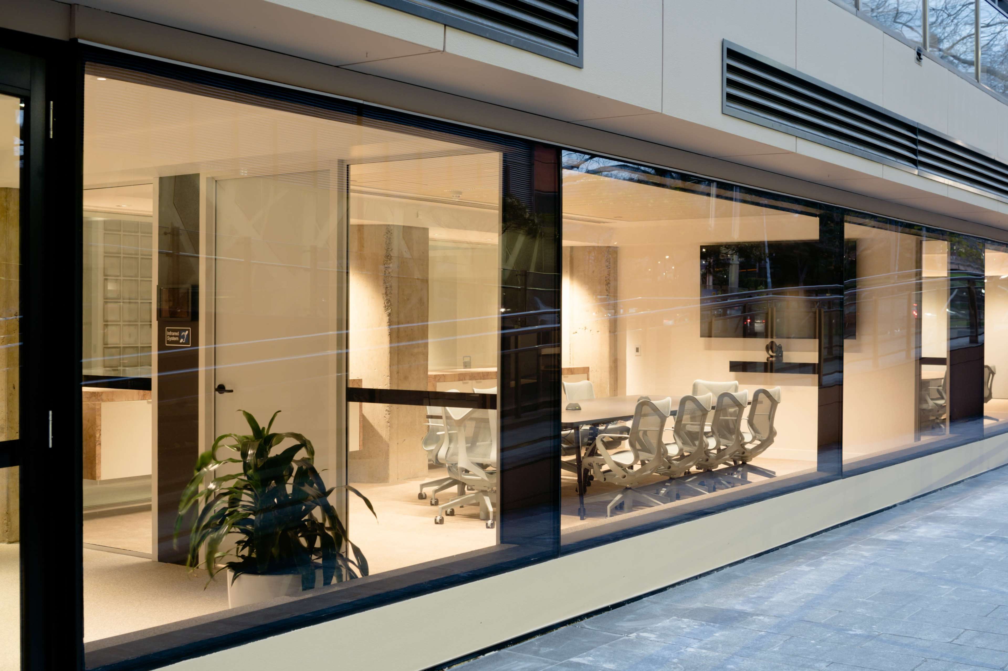 A modern office conference room with glass walls, a long table, and ergonomic chairs, visible from the exterior.