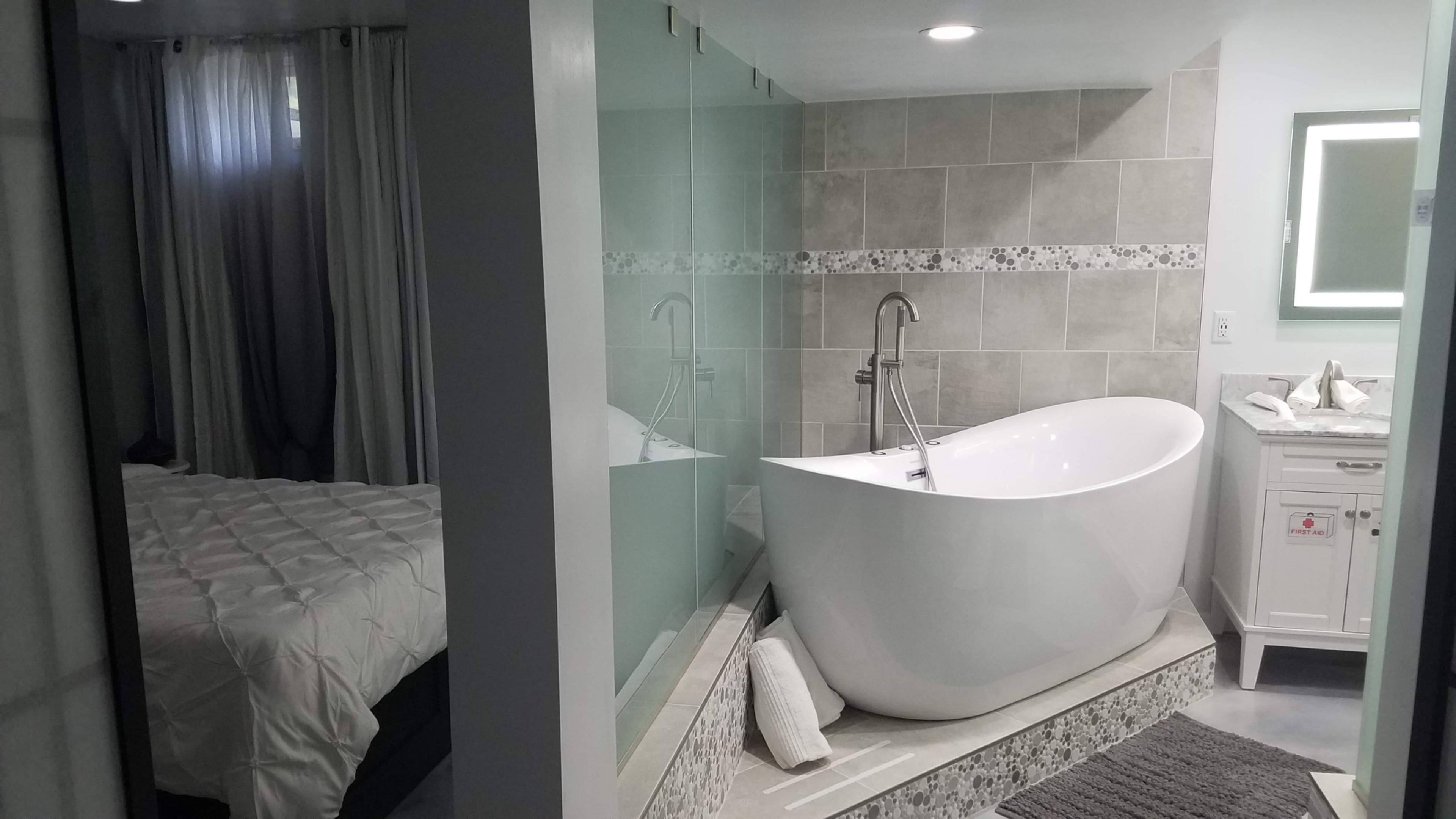 A modern bathroom with a freestanding bathtub and a separate area featuring a bed and curtains.