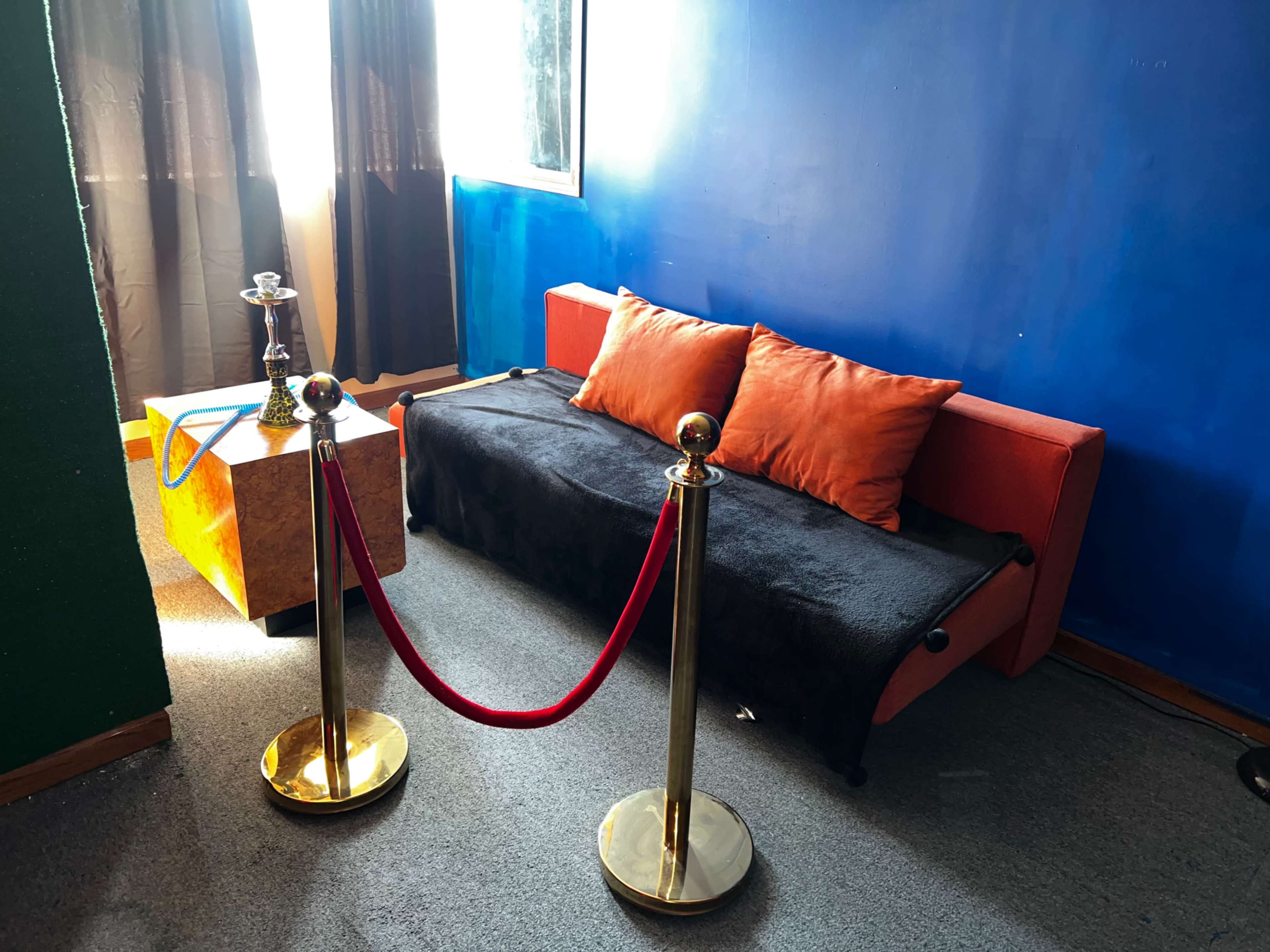 A seating area with an orange couch covered in a black blanket, a small table, and a red rope barrier in front.