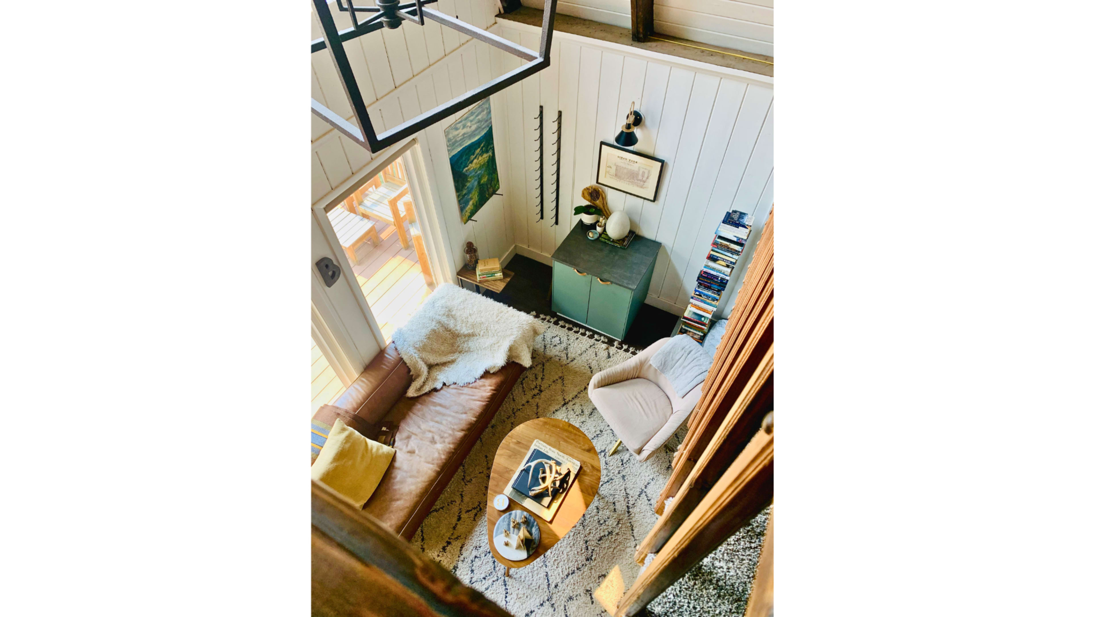 The image shows an overhead view of a cozy living room with a brown leather sofa, a round coffee table, and bookshelves against the wall.