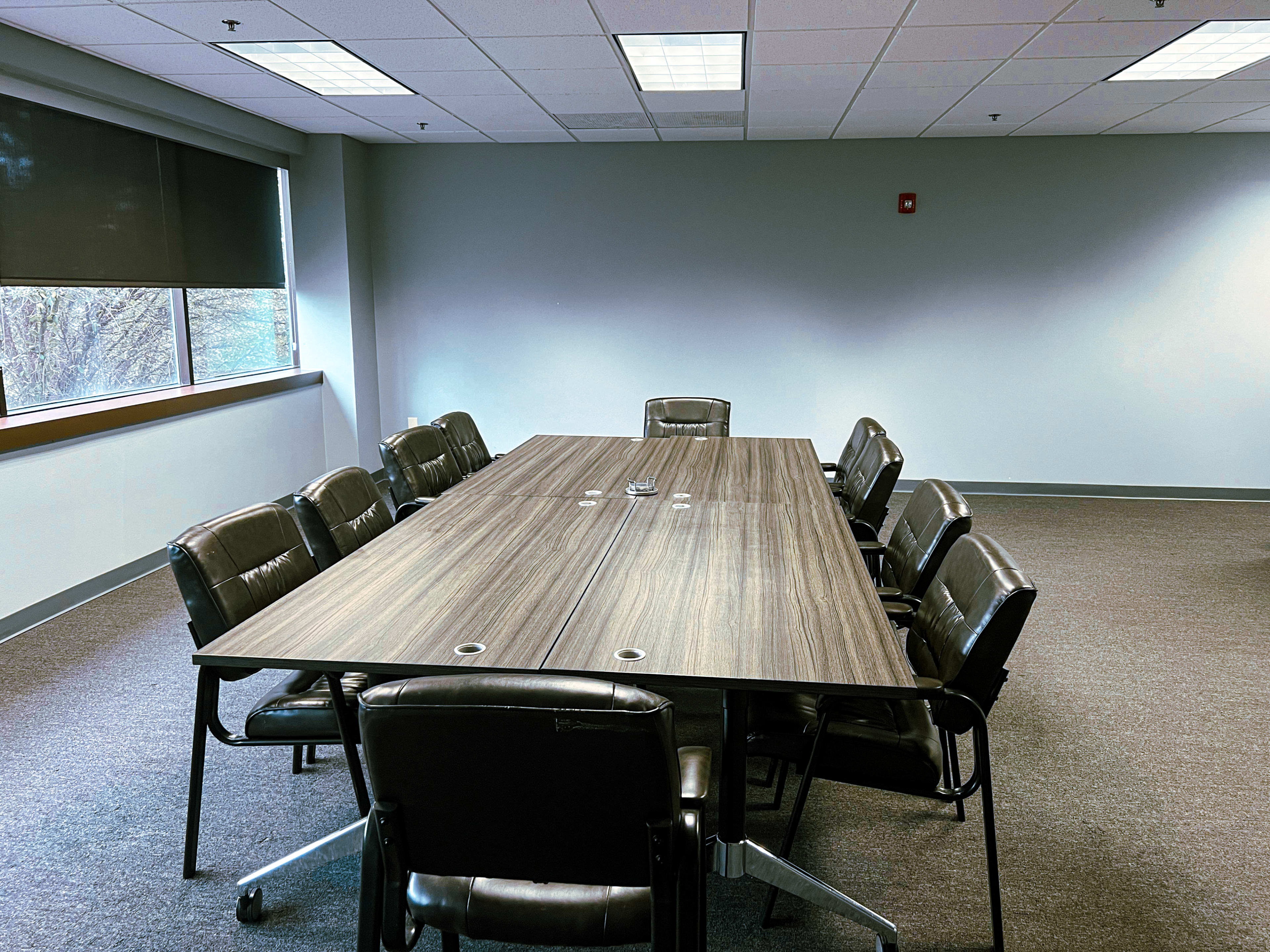 A conference room with a long wooden table surrounded by eight black leather chairs.