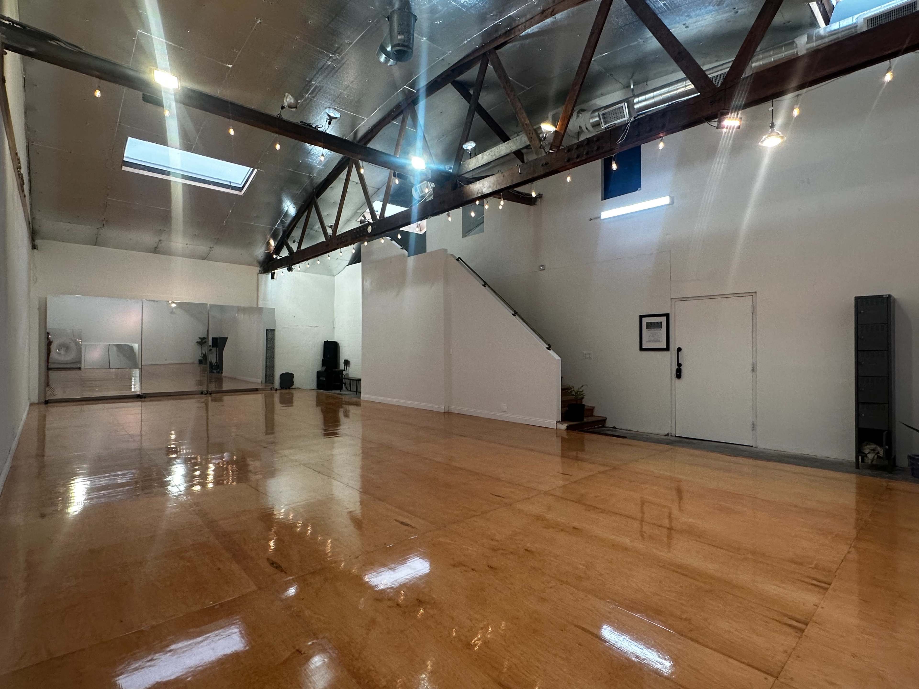 The image shows a spacious, well-lit interior with polished wooden flooring, large windows, and exposed beams.