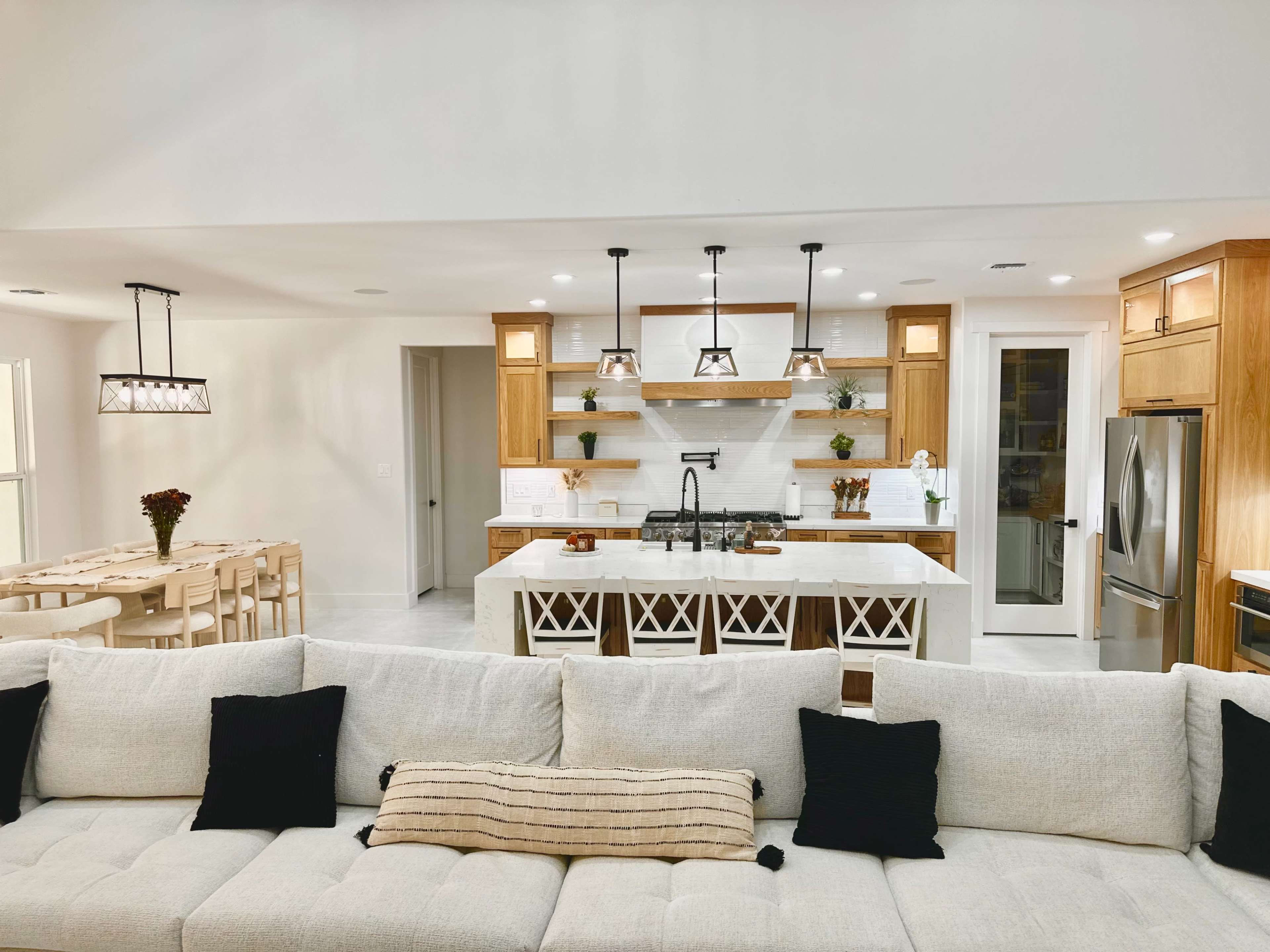The image shows a modern kitchen with wooden cabinetry, white countertops, and a spacious dining area visible in the background.