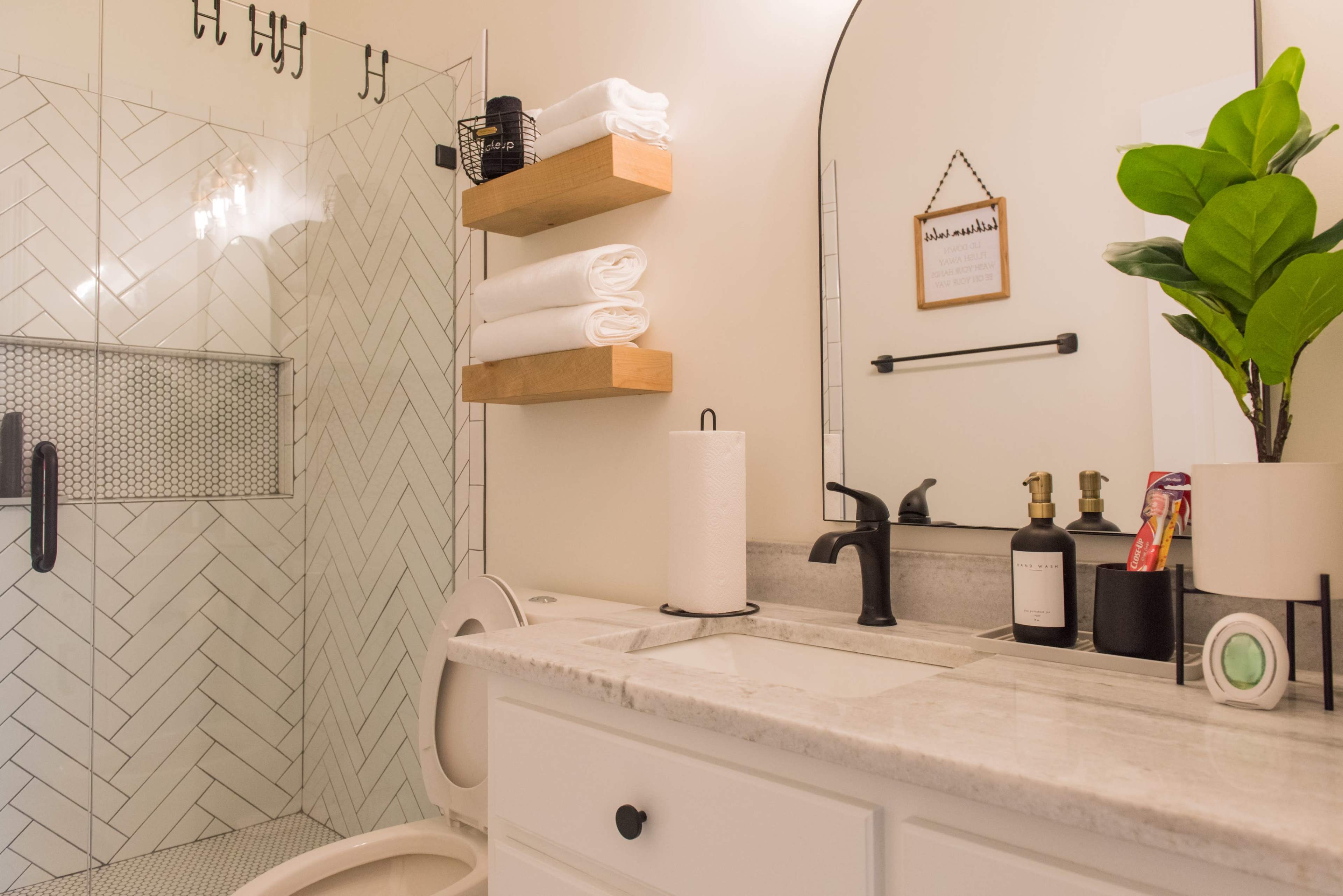 A modern bathroom featuring a glass shower, a stone countertop with a sink, neatly arranged towels, and a potted plant.