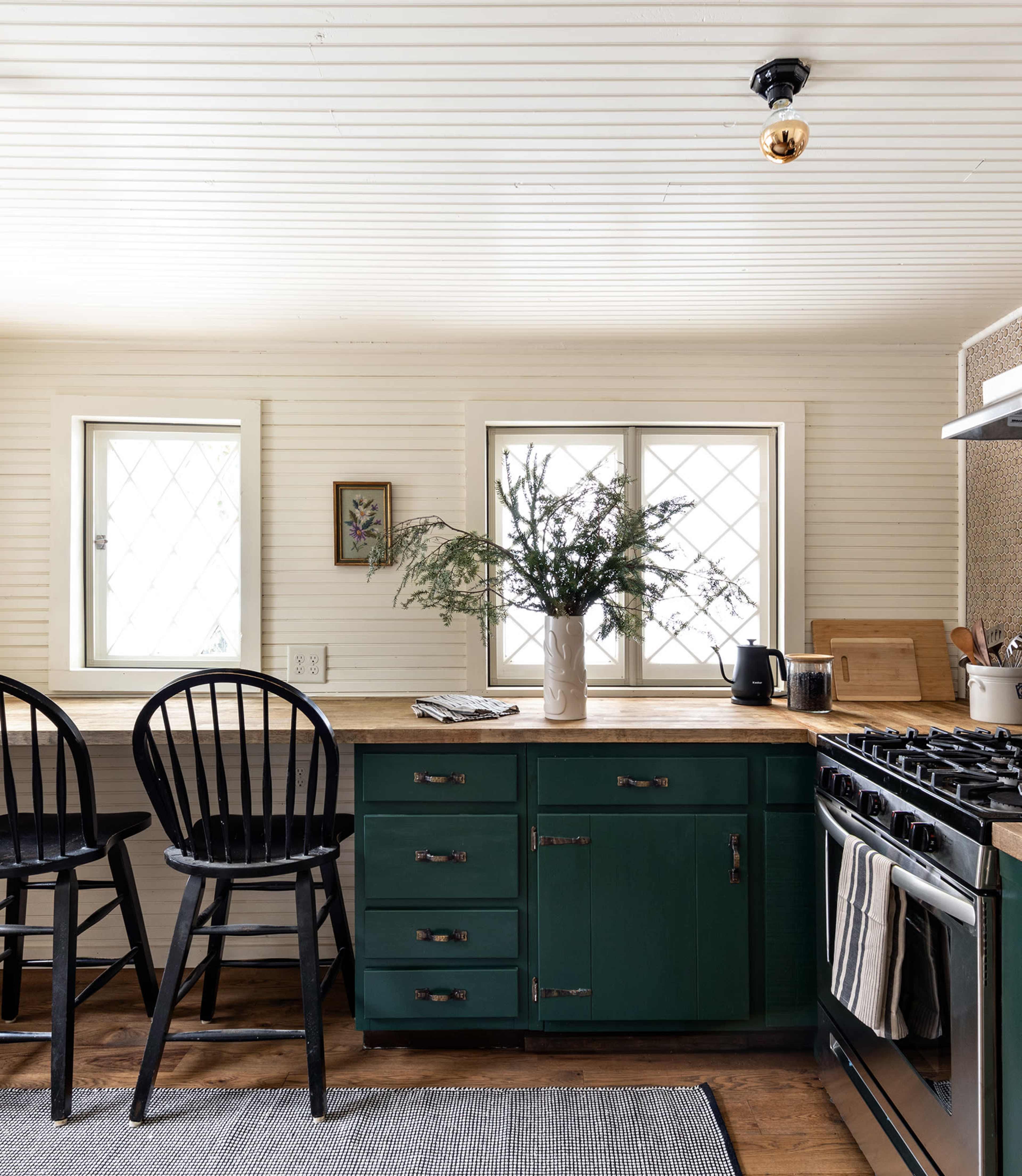 The kitchen features a wooden countertop, dark green cabinetry, and two black chairs by a bright window.