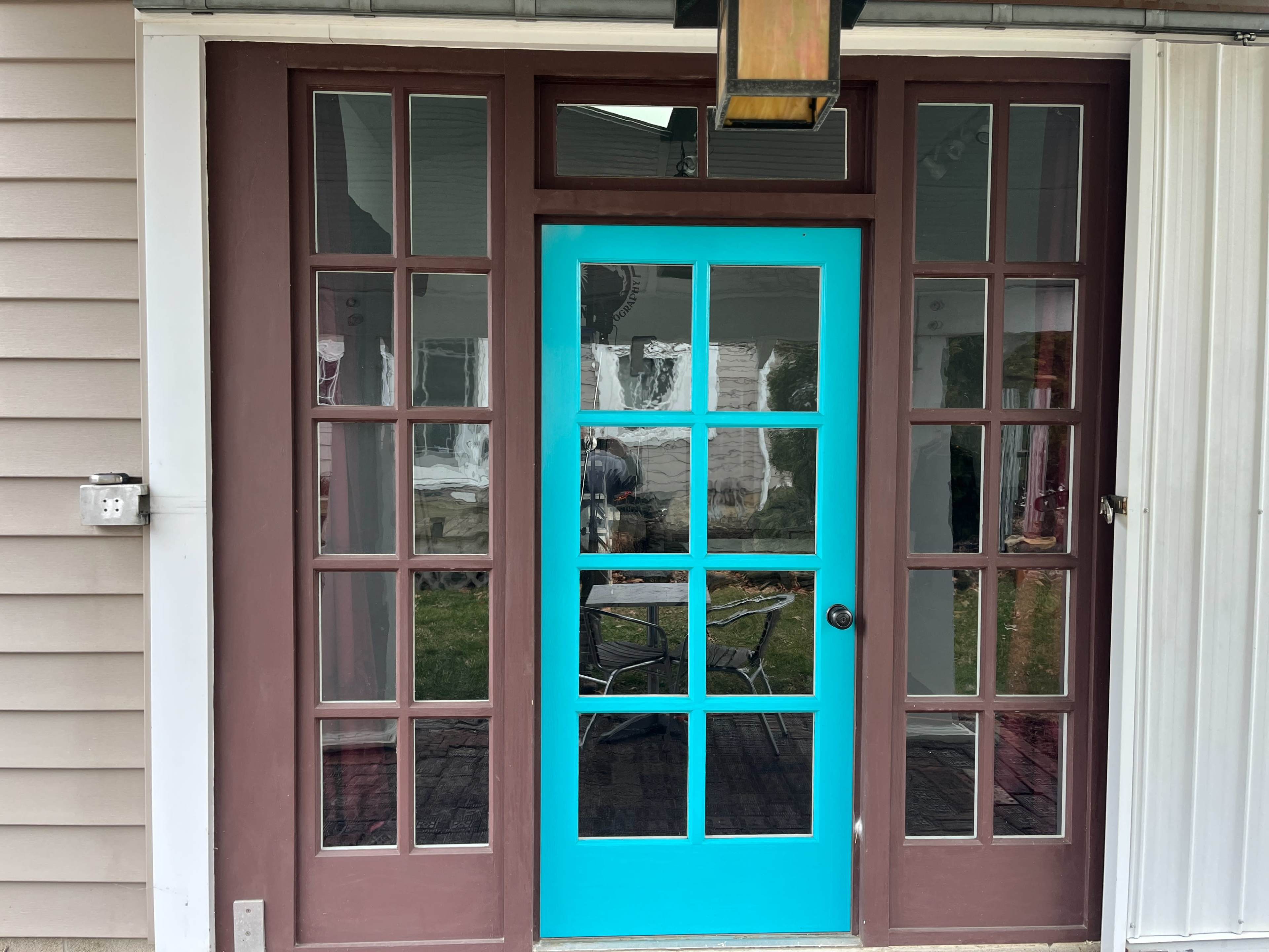 A front door painted turquoise, framed by brown wooden panels and glass windows, leading to a covered porch area.