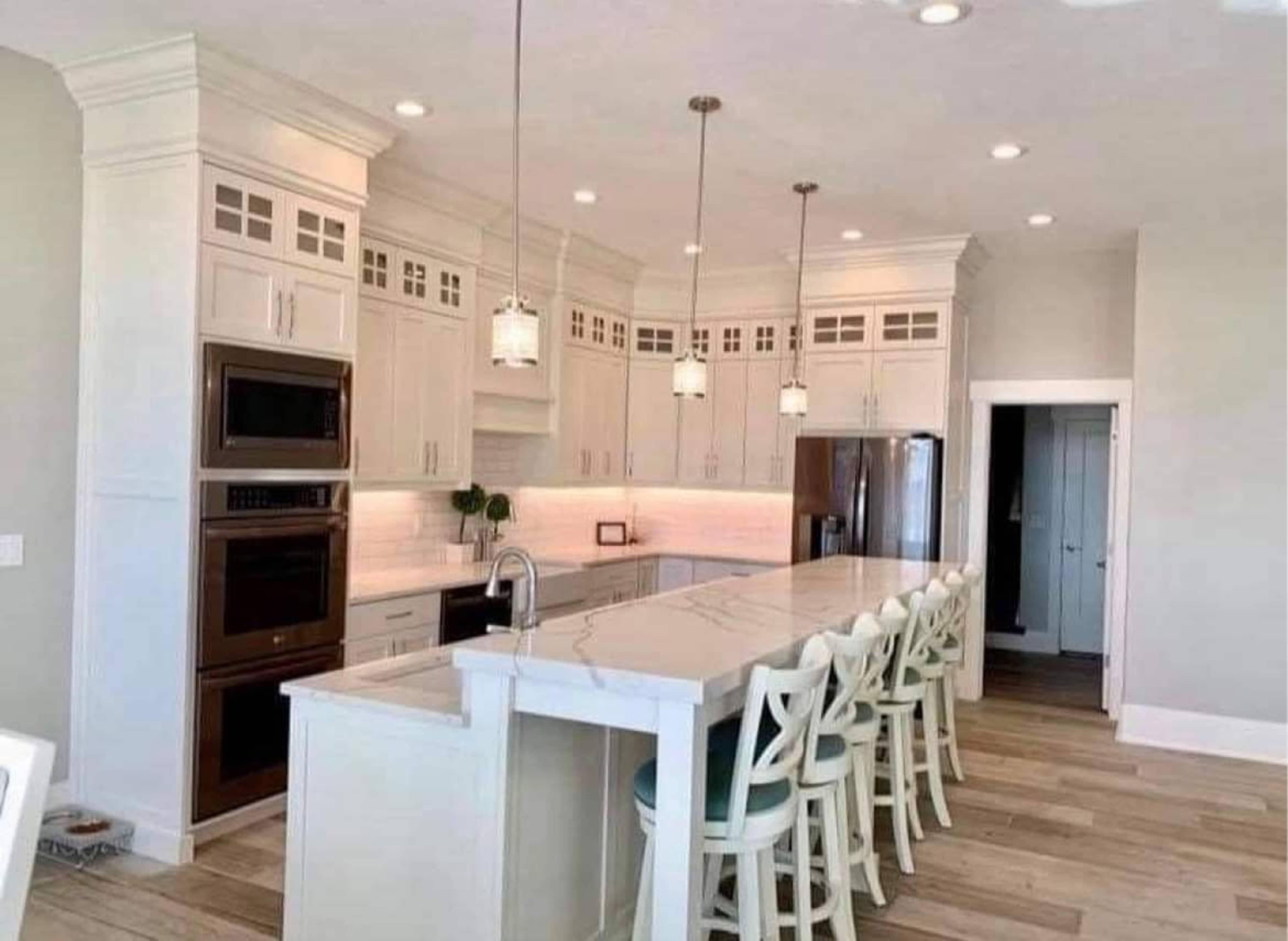 A modern kitchen features white cabinetry, a large marble island with seating, and stainless steel appliances.
