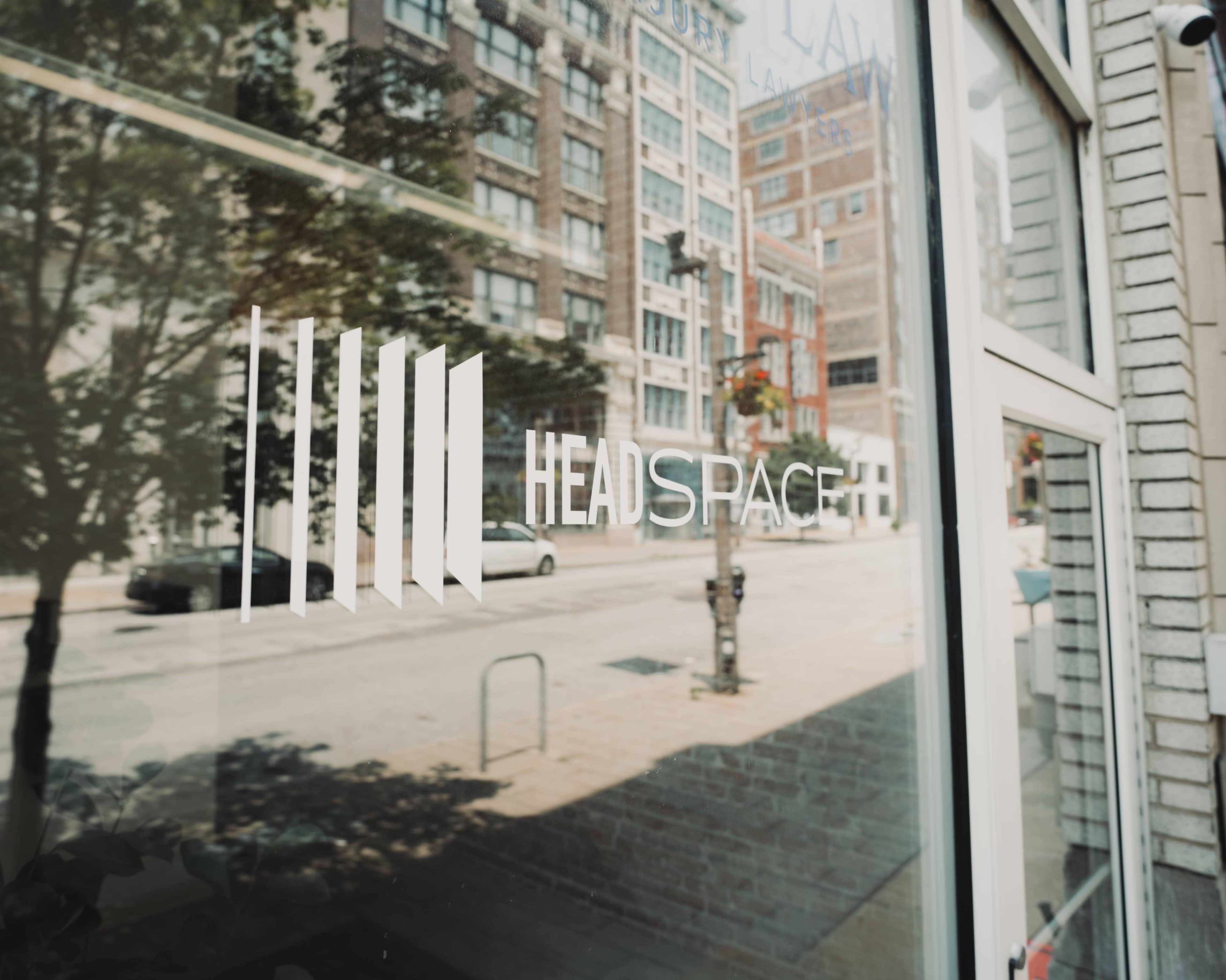 The image shows the reflection of a city street in the glass window of a building with a sign that reads "HEADSPACE."