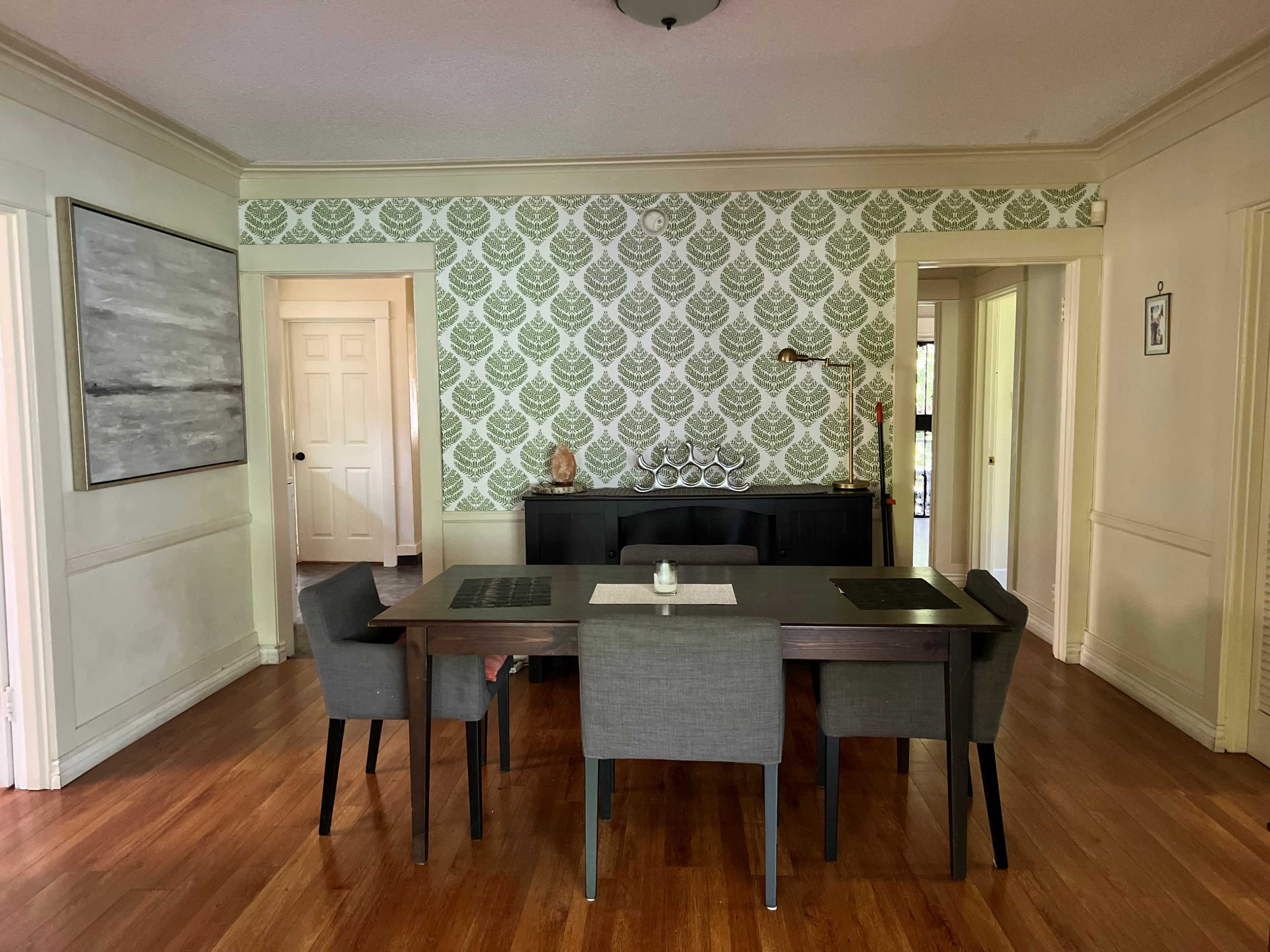 A dining area with a wooden table and gray chairs, set against a patterned green wallpaper.