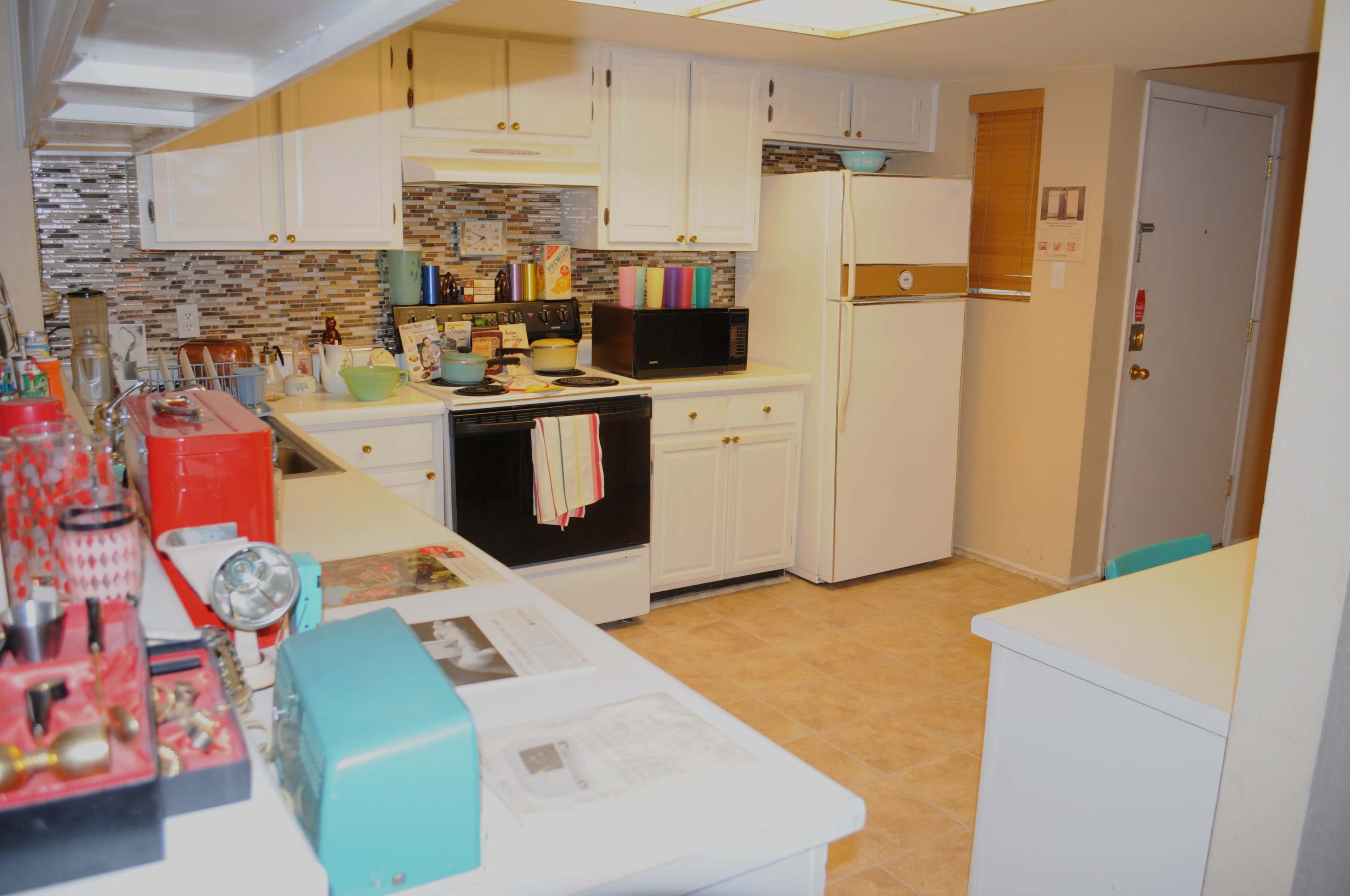 A well-lit kitchen features white cabinets, a tiled backsplash, and various appliances including a stove, microwave, and refrigerator.