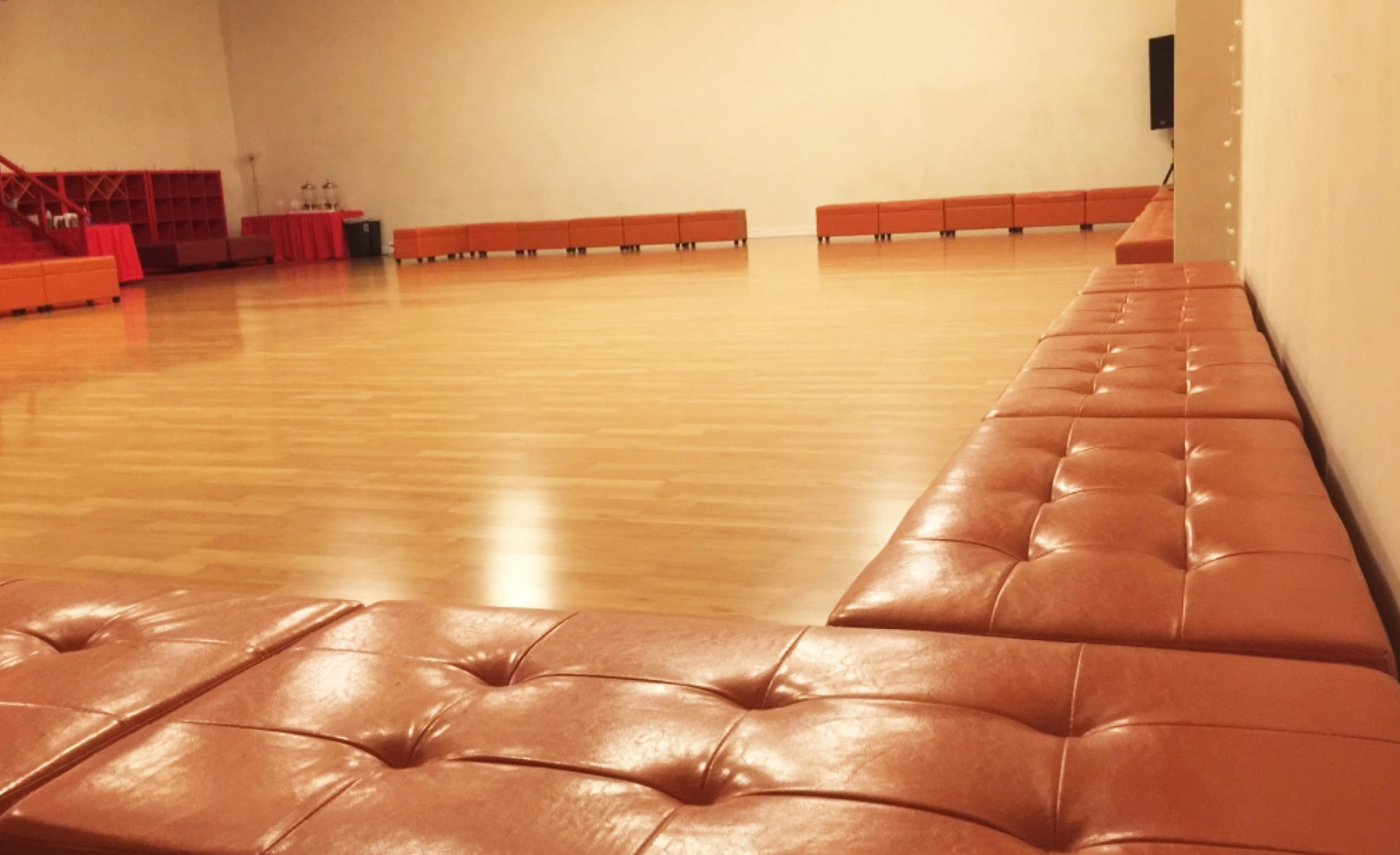 A spacious indoor area with a smooth wooden floor and an arrangement of orange cushions along one side.