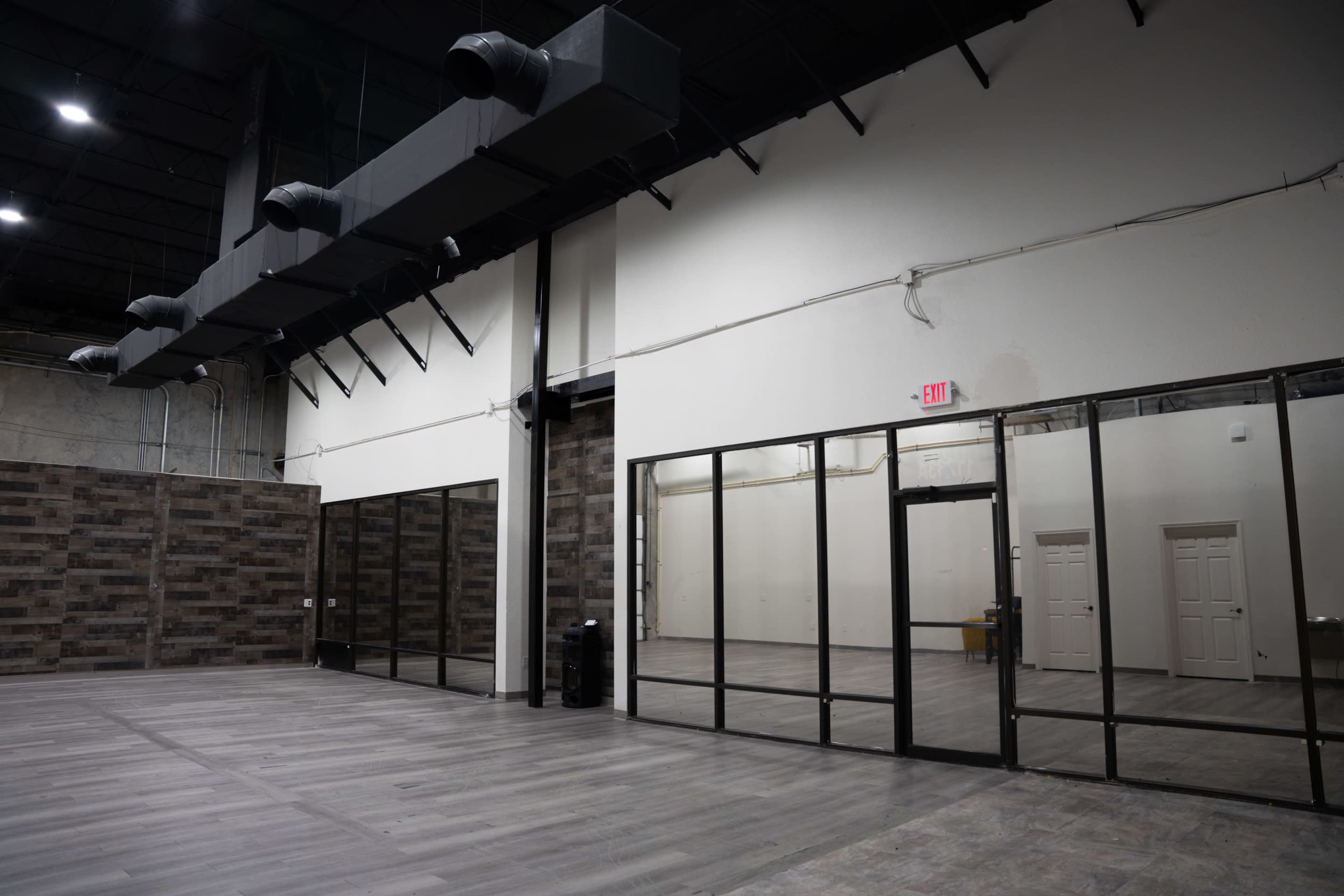 An empty industrial-style interior space with high ceilings, large windows on one wall, and exposed ductwork.