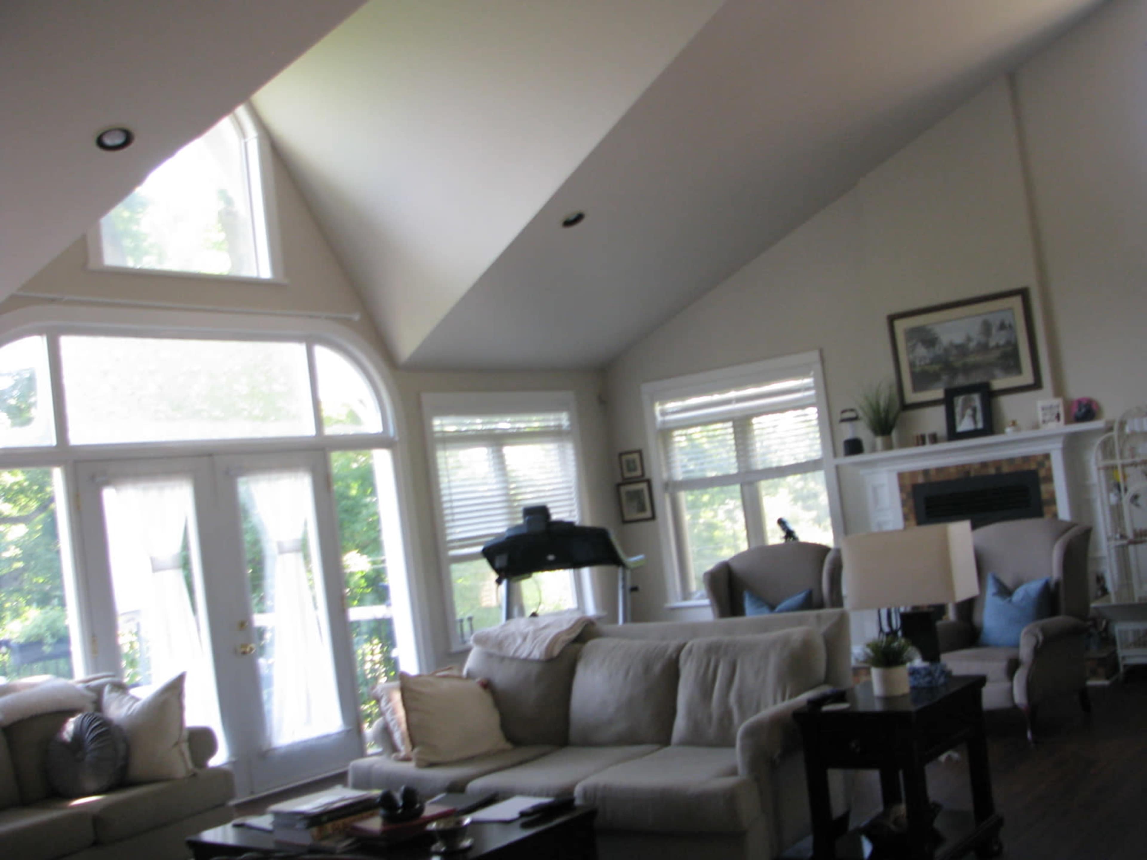 A spacious living room with high vaulted ceilings, large windows, and a mix of light-colored furniture.