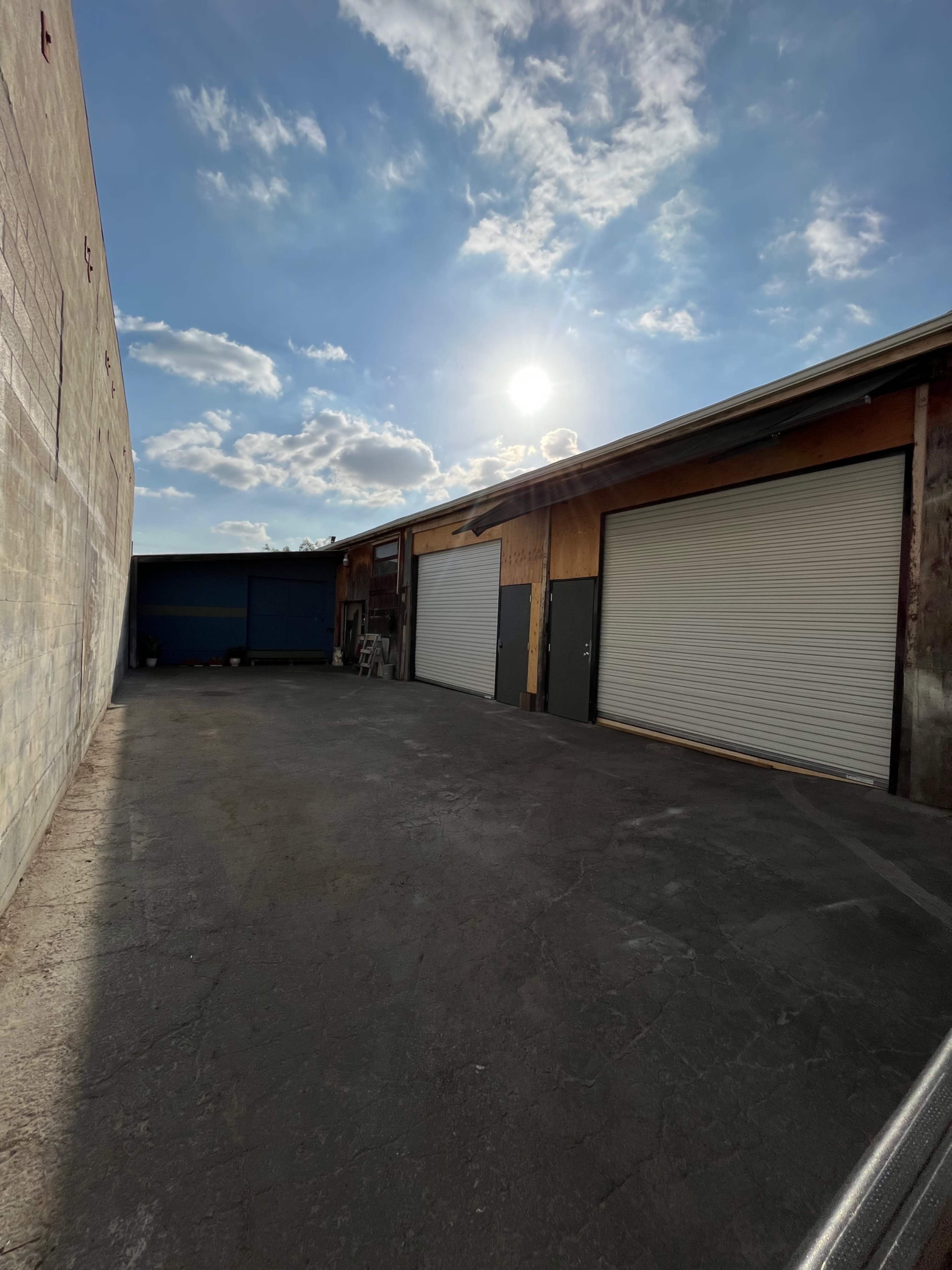 A partially enclosed industrial area with two closed garage doors and a bright sun in the sky.