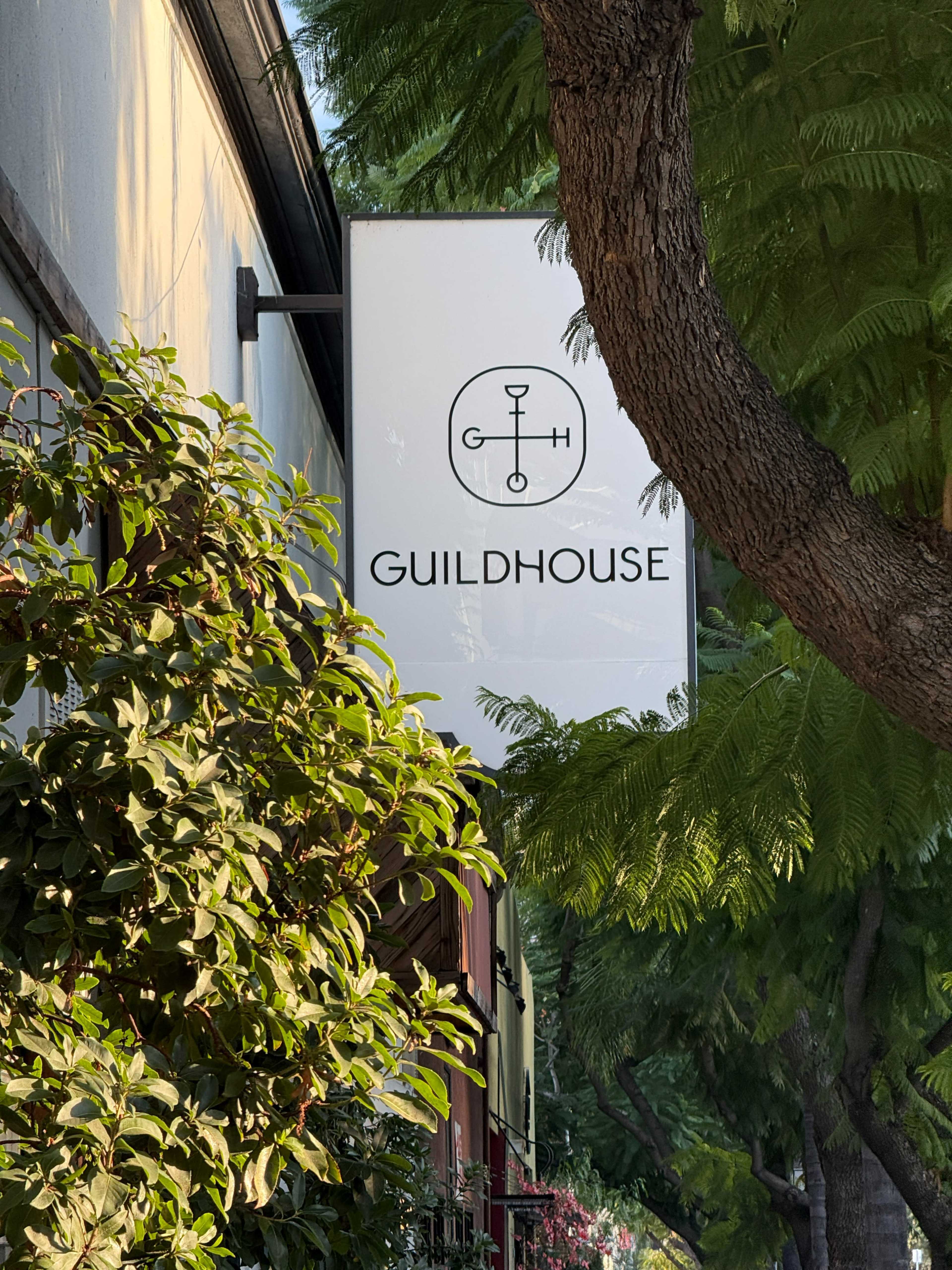 A sign reading "GUILDHOUSE" is suspended from a building, partially obscured by trees and foliage.