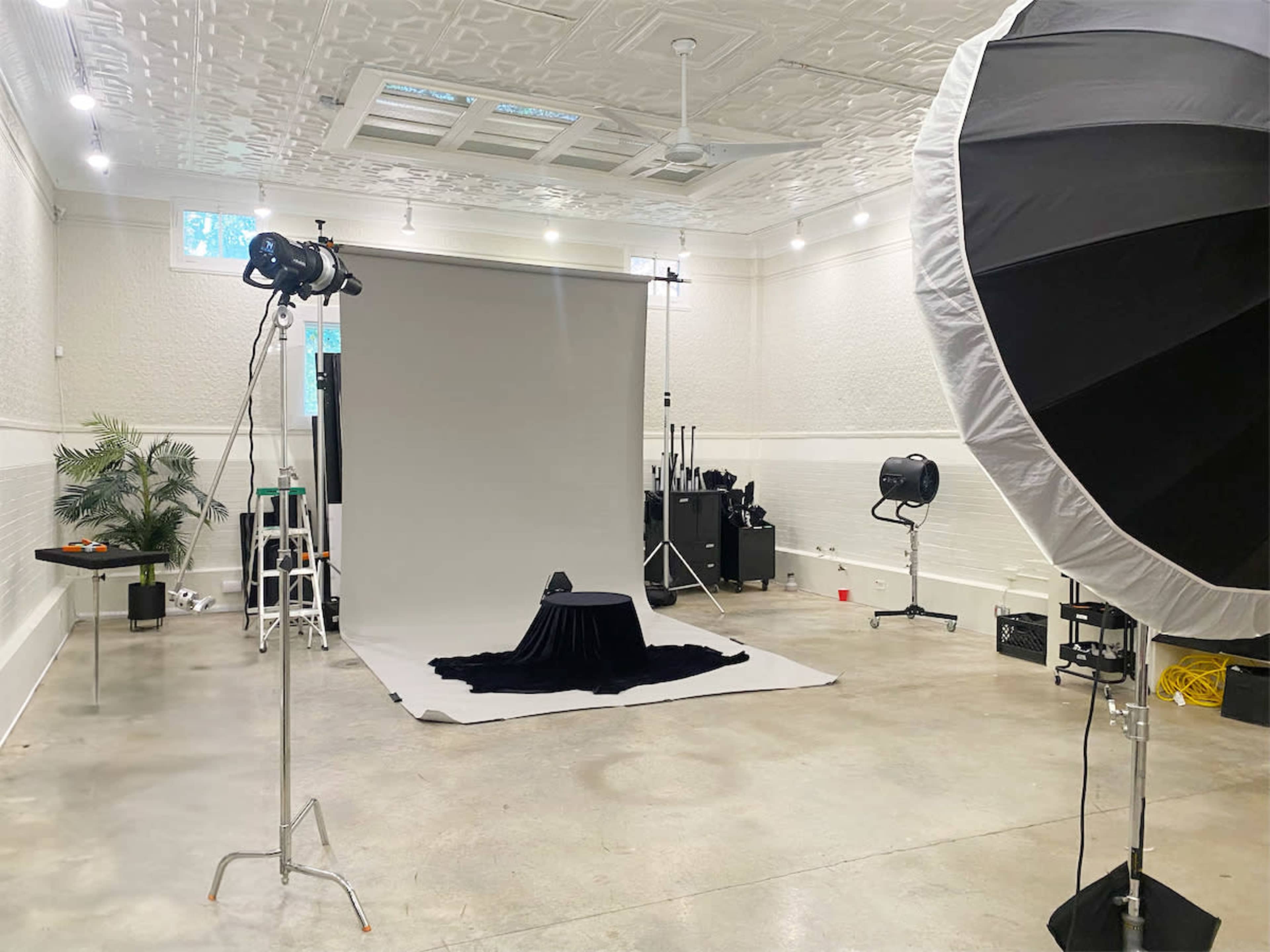A photography studio with a backdrop, lighting equipment, and a black cloth draped over a small table.
