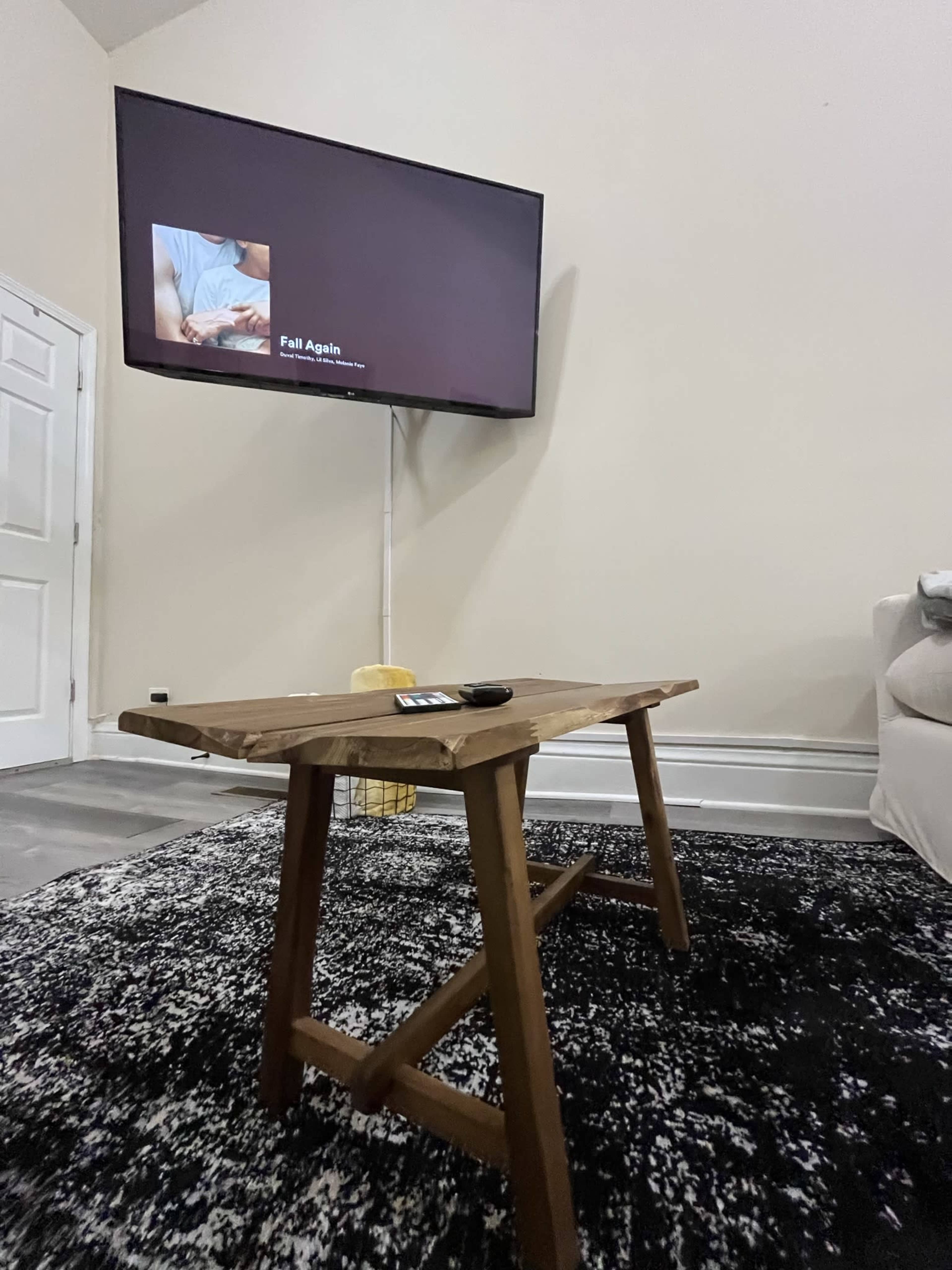 A wooden table sits on a black and white patterned rug, with a television displaying content in the background.