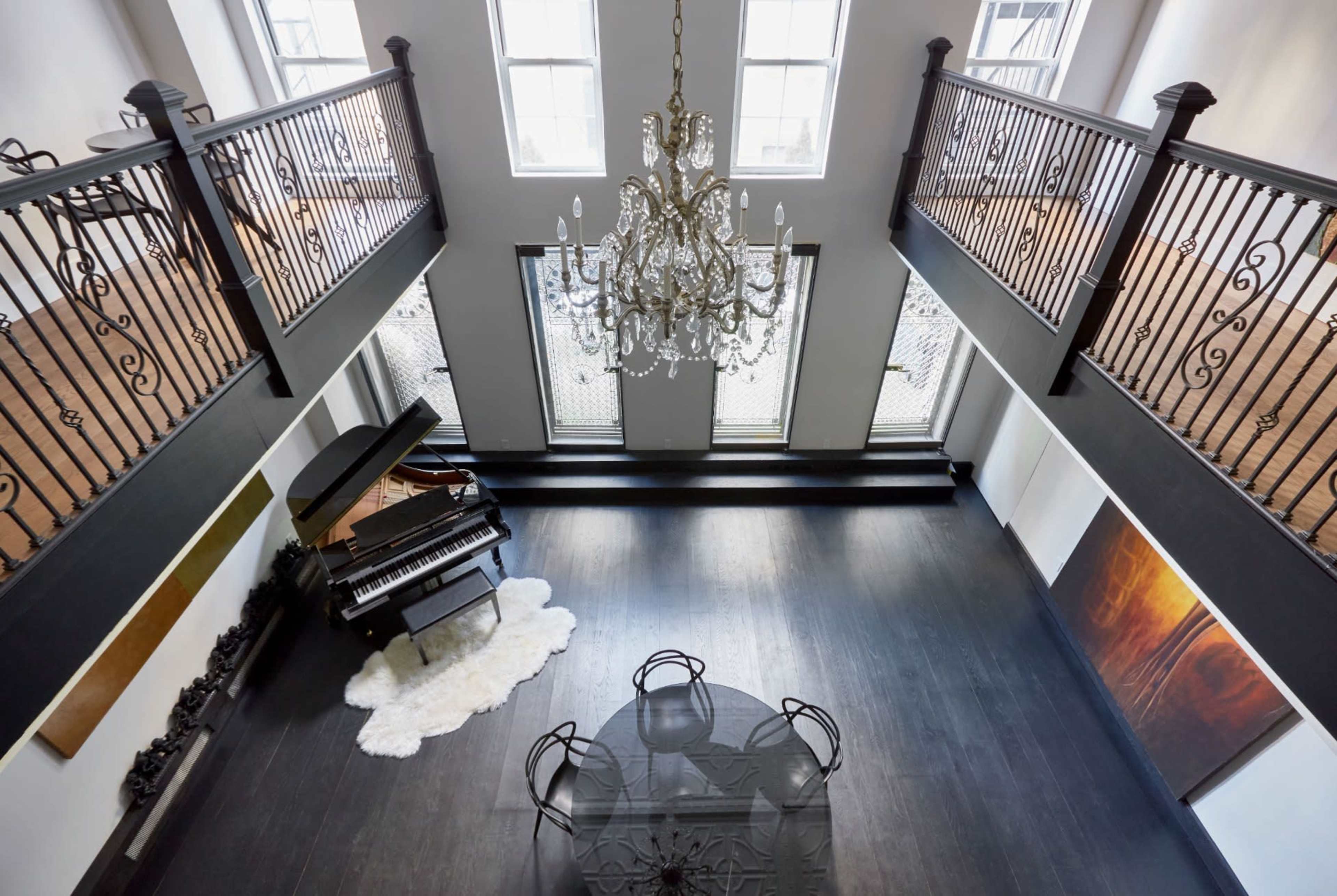 A spacious, modern interior with a grand chandelier, a piano on one side, and a glass dining table centered in the room.