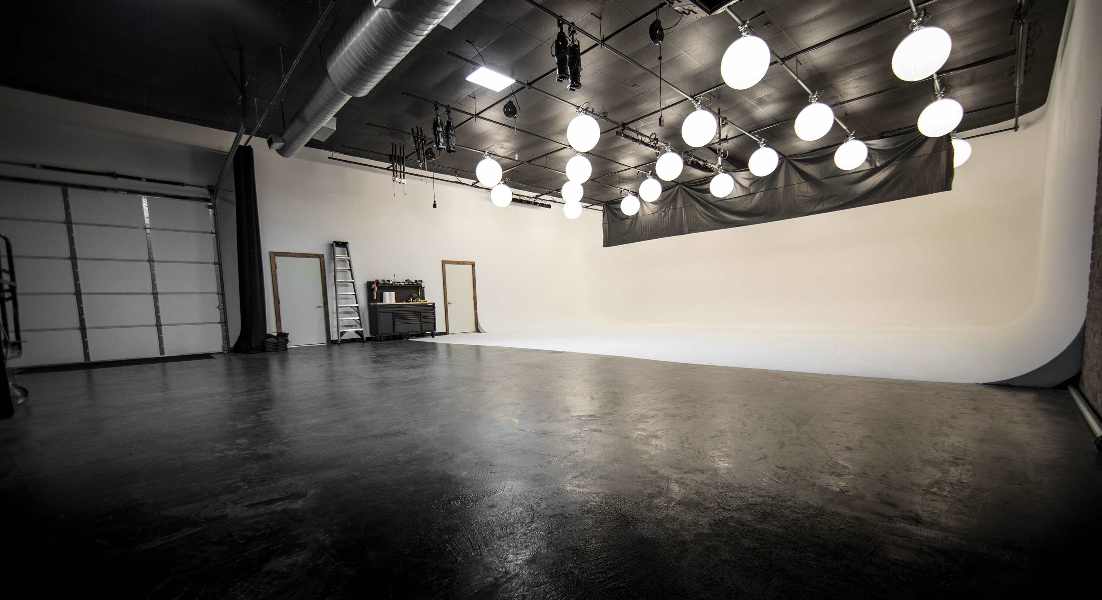 An empty photography studio with a large white backdrop and multiple overhead lights.