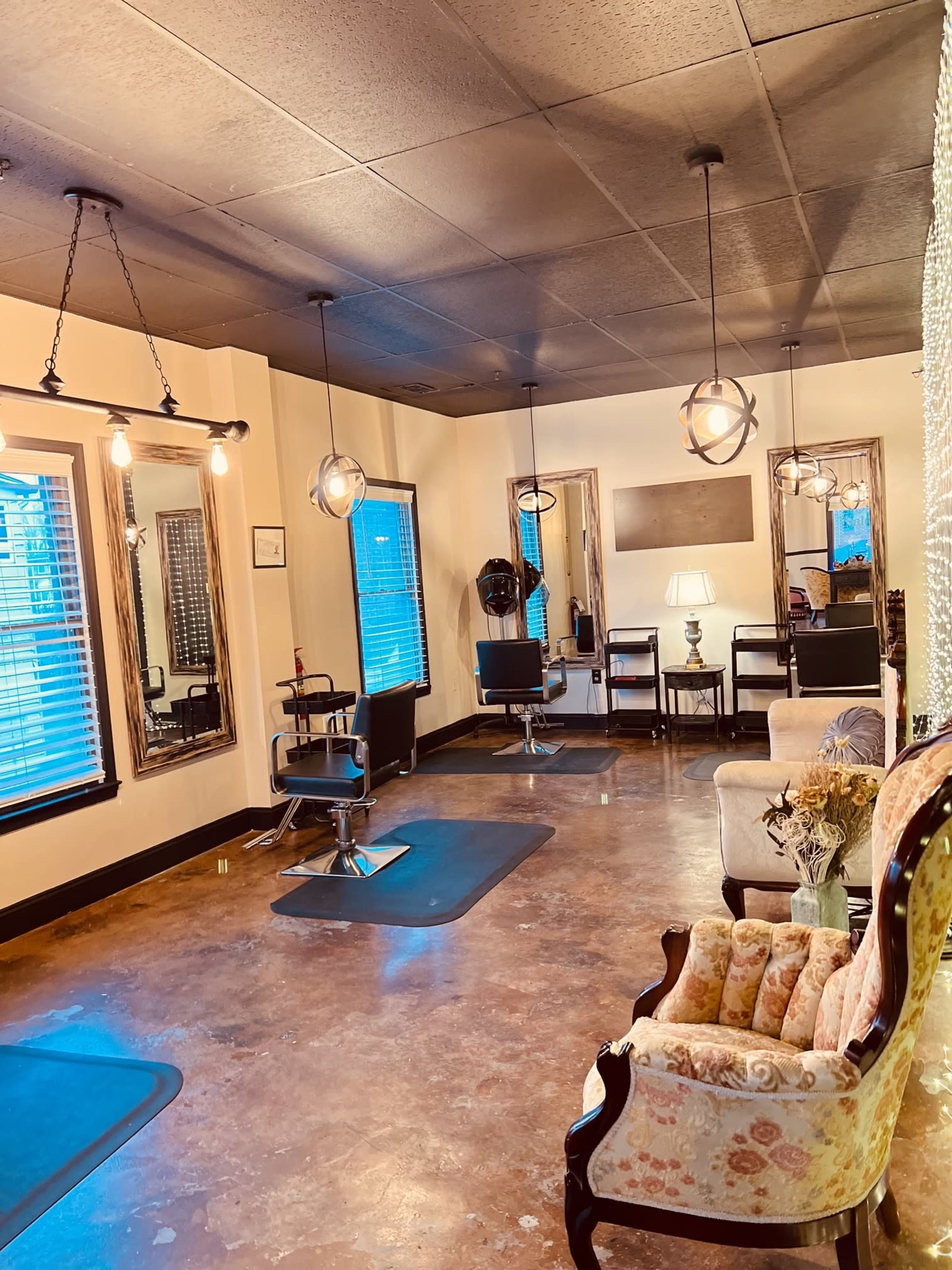 The image shows a hair salon interior featuring chairs, mirrors, and decorative lighting, with a vintage couch in the corner and windows allowing natural light.