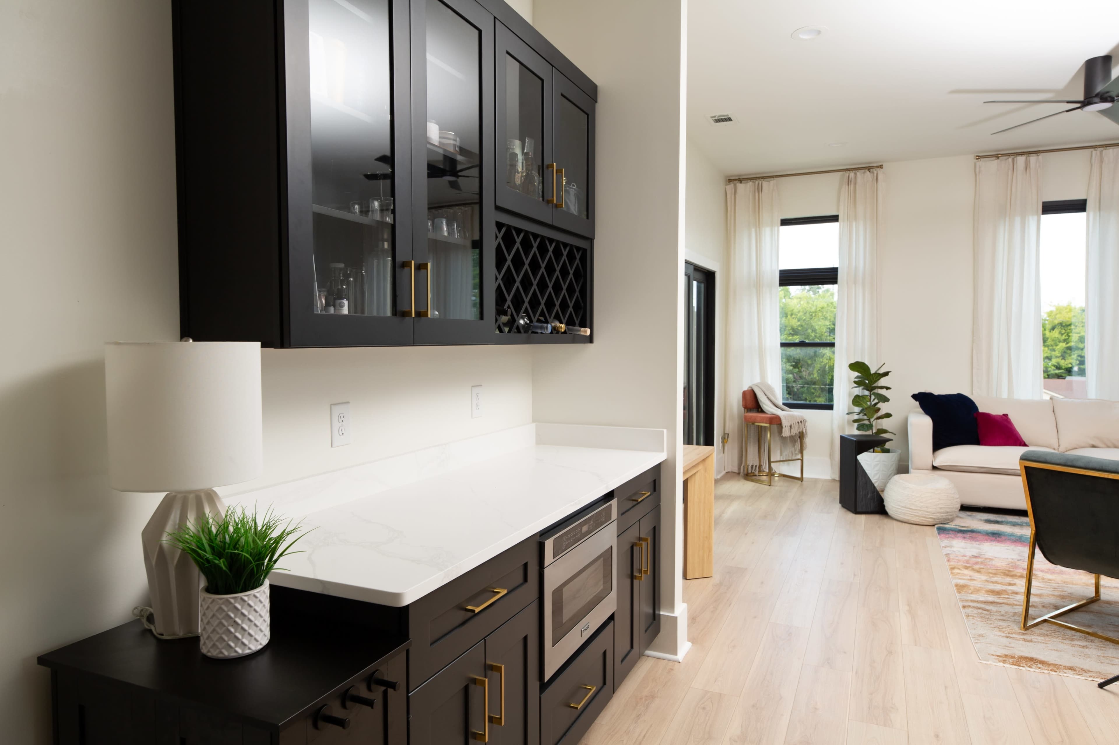 The image showcases a modern kitchen space with dark cabinetry, a white countertop, and a neatly arranged living area in the background.