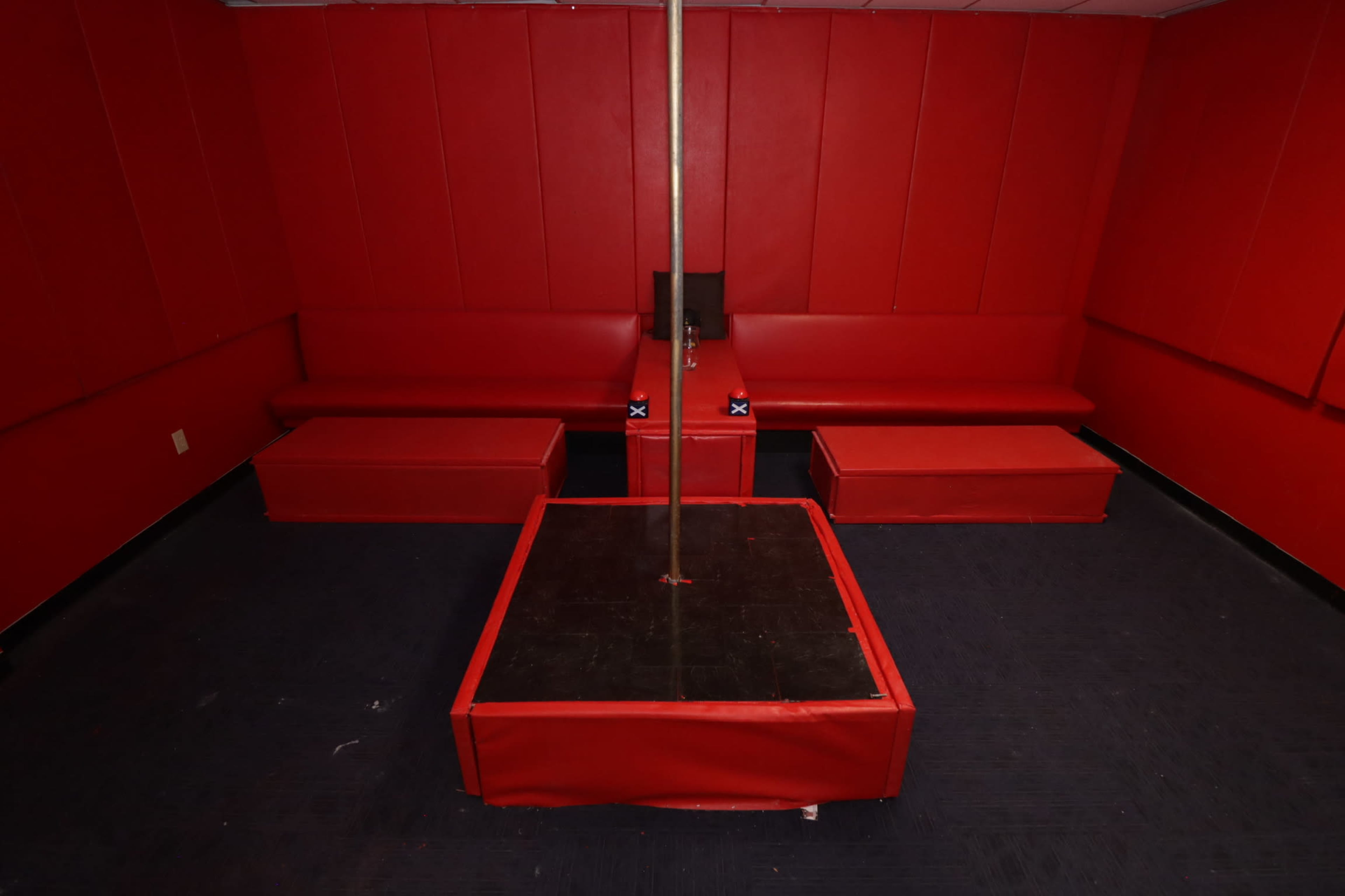 A small room with red walls and seating, featuring a central pole mounted on a square platform.