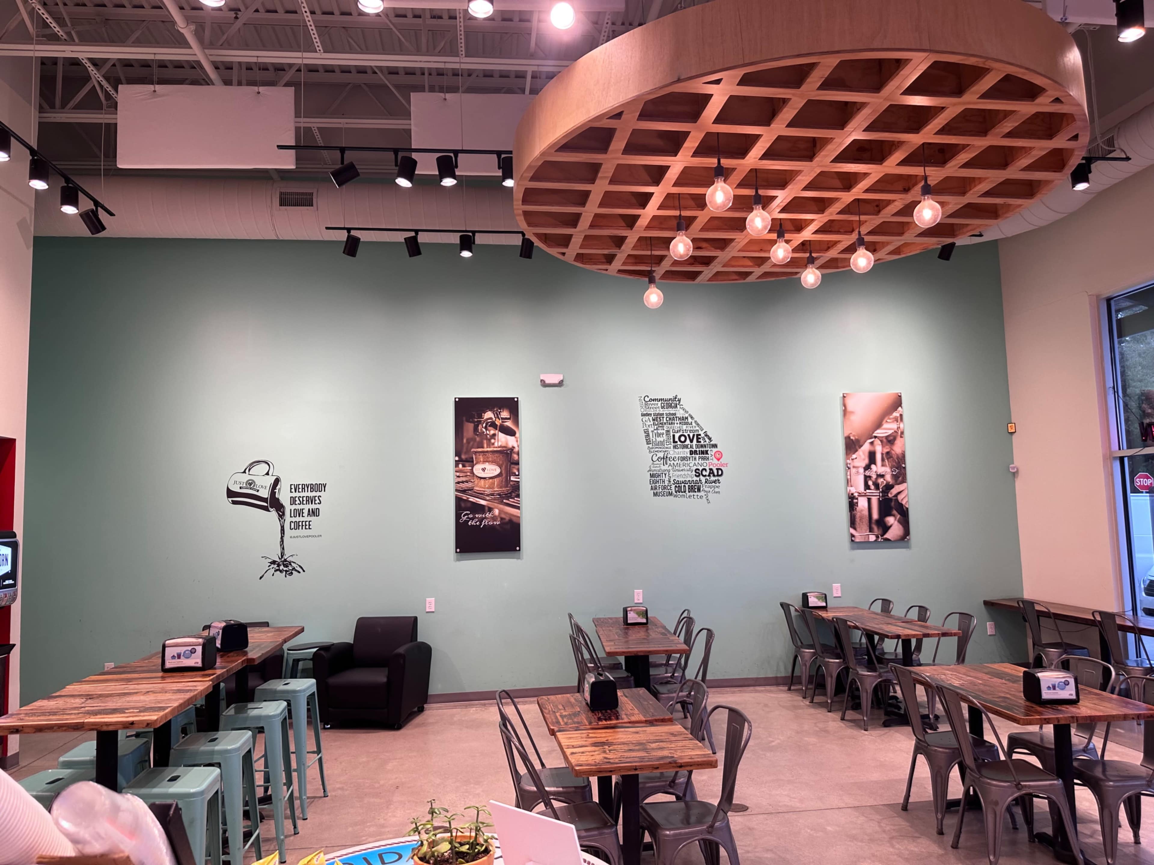 A modern café interior with teal walls, wooden tables, metal chairs, and framed wall art.